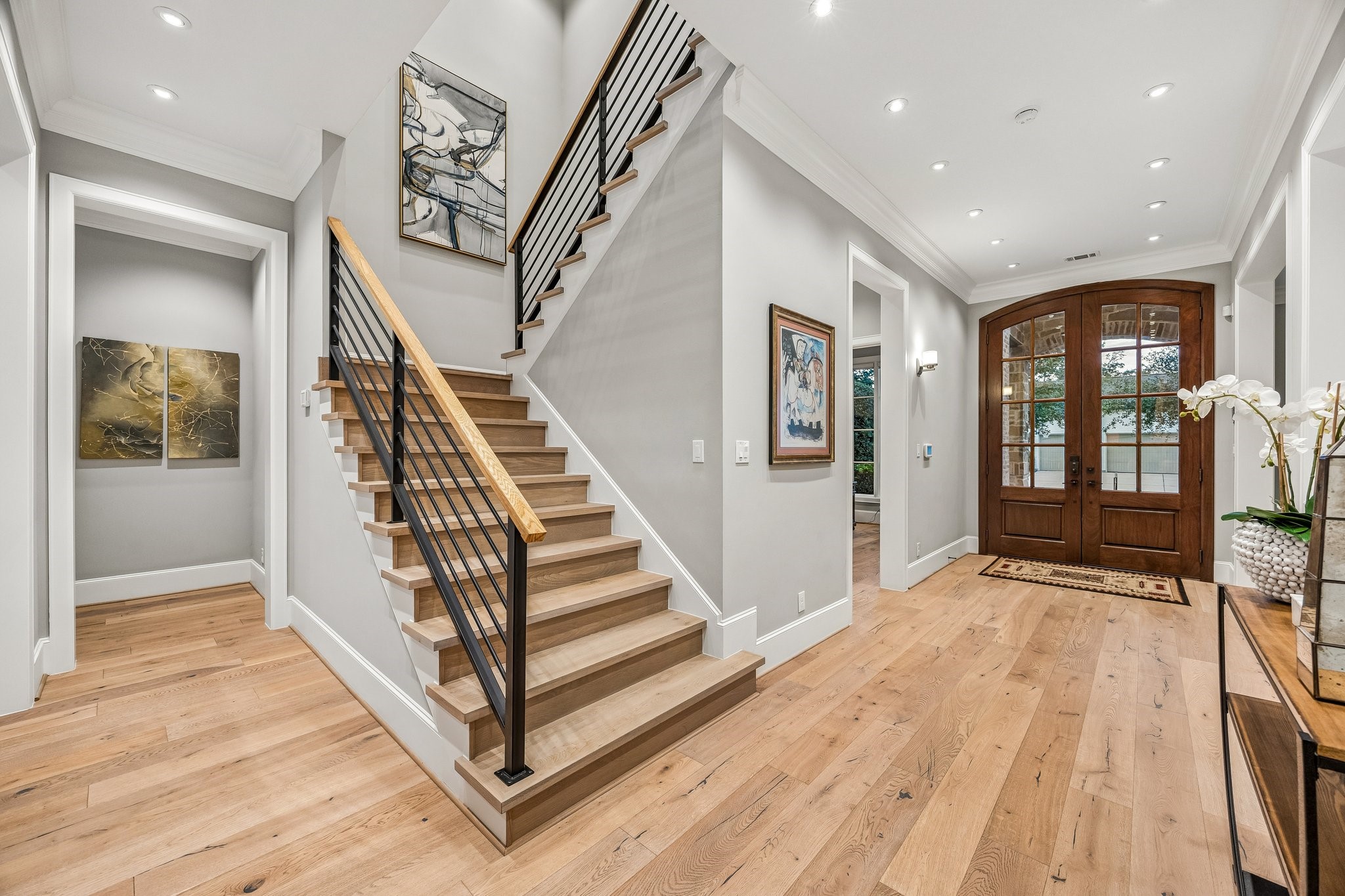 This stunning entry foyer showcases a beautiful blend of contemporary architectural design and timeless elegance. A striking staircase serves as the architectural focal point, featuring natural wood treads, sleek black horizontal iron railings, and a coordinating wood handrail, creating a sophisticated contrast of materials and textures.