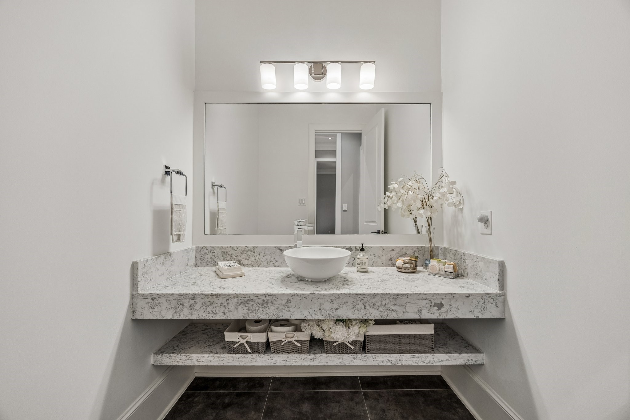 This beautifully appointed powder room showcases a stunning floating marble vanity, white vessel sink and sleek polished chrome fixtures. Rich charcoal-toned tile flooring provides a beautiful contrast to the crisp white walls and light marble finishes, adding depth and sophistication.