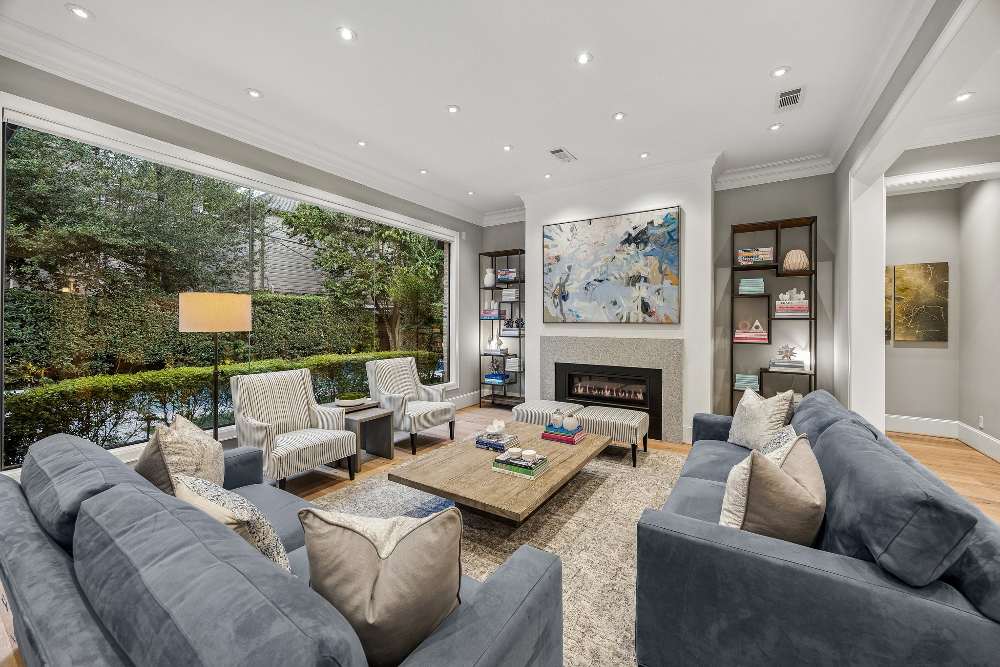 Another view of the living room, which also features, LED recessed lighting, wide plank floors, crown molding and 8 Inch baseboards.  There is also a direct vent, sleek linear fireplace framed by a contemporary stone surround.