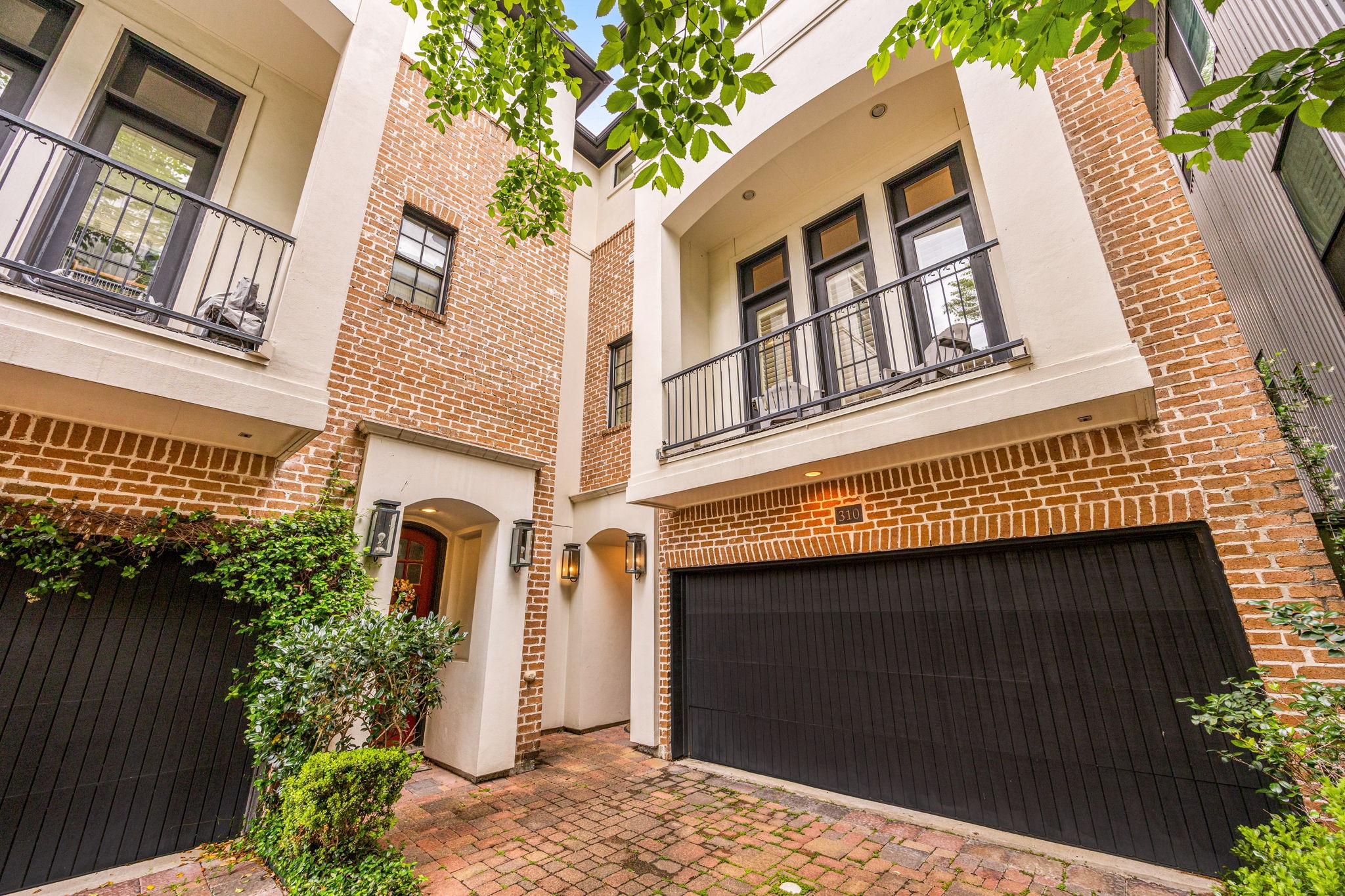 In the heart of Montrose, 310 W Bell is a charming three-story home with a traditional brick and stucco facade. It features a small balcony, a two-car garage, and a quaint courtyard with lush greenery, creating a welcoming and stylish exterior.