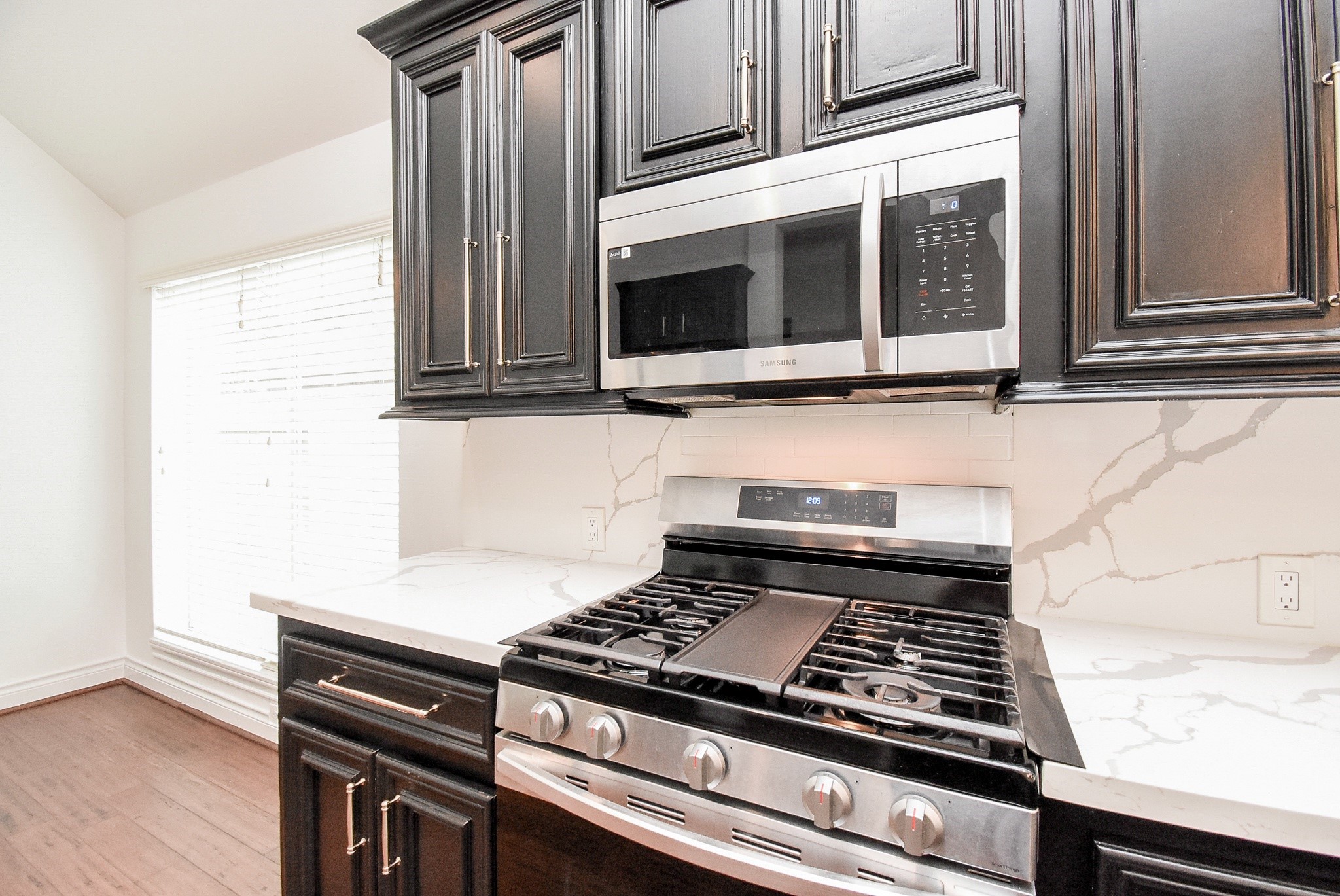 Prepare your favorite meals in this beautifully appointed kitchen featuring a gas cooktop and oven, stainless steel appliances, rich cabinetry, quartz countertops, and a timeless designer backsplash.