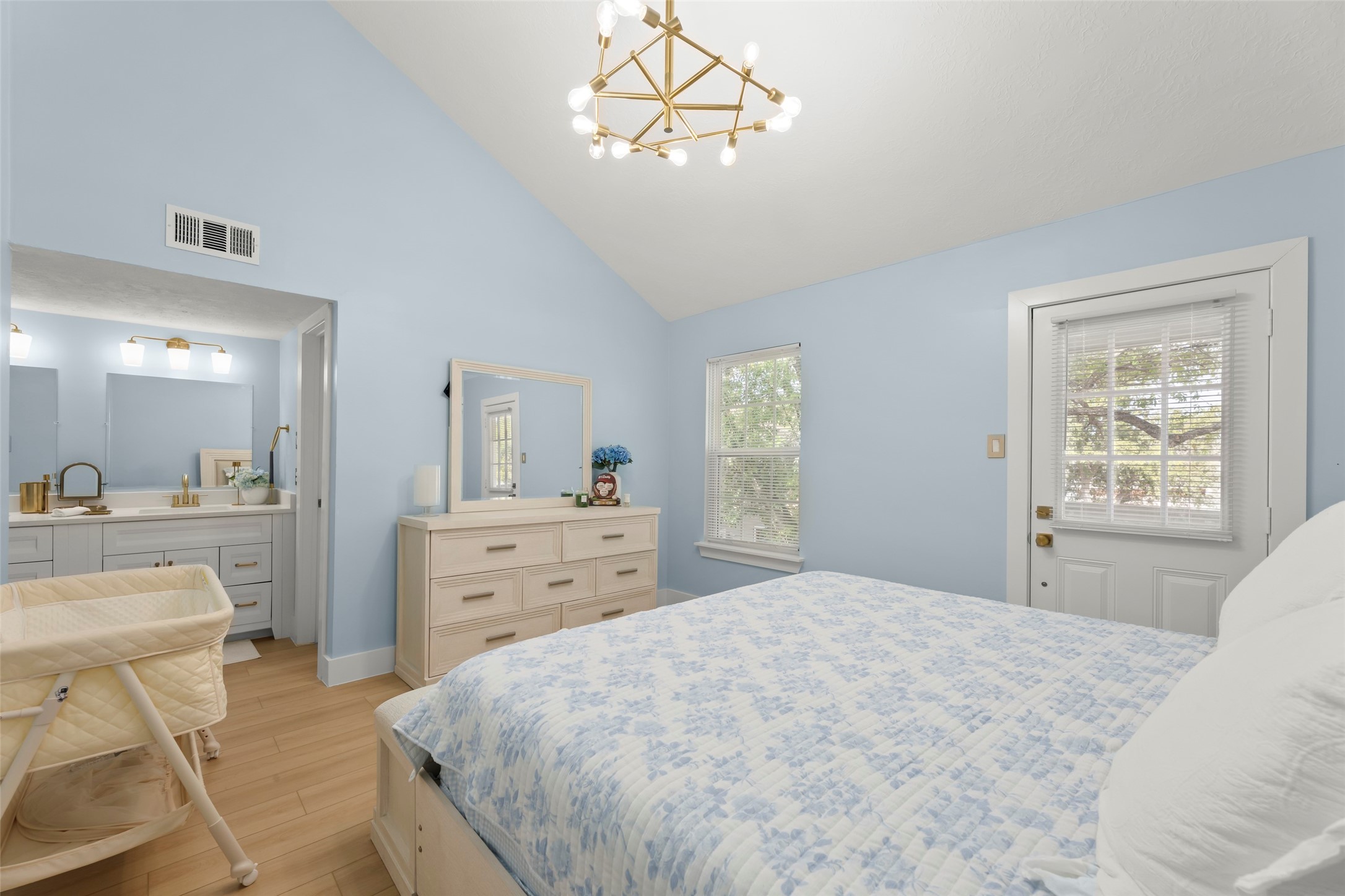 Discover a serene bedroom retreat with soft blue walls, elegant chandelier, and seamless flow into a stylish en-suite bathroom, perfect for unwinding.