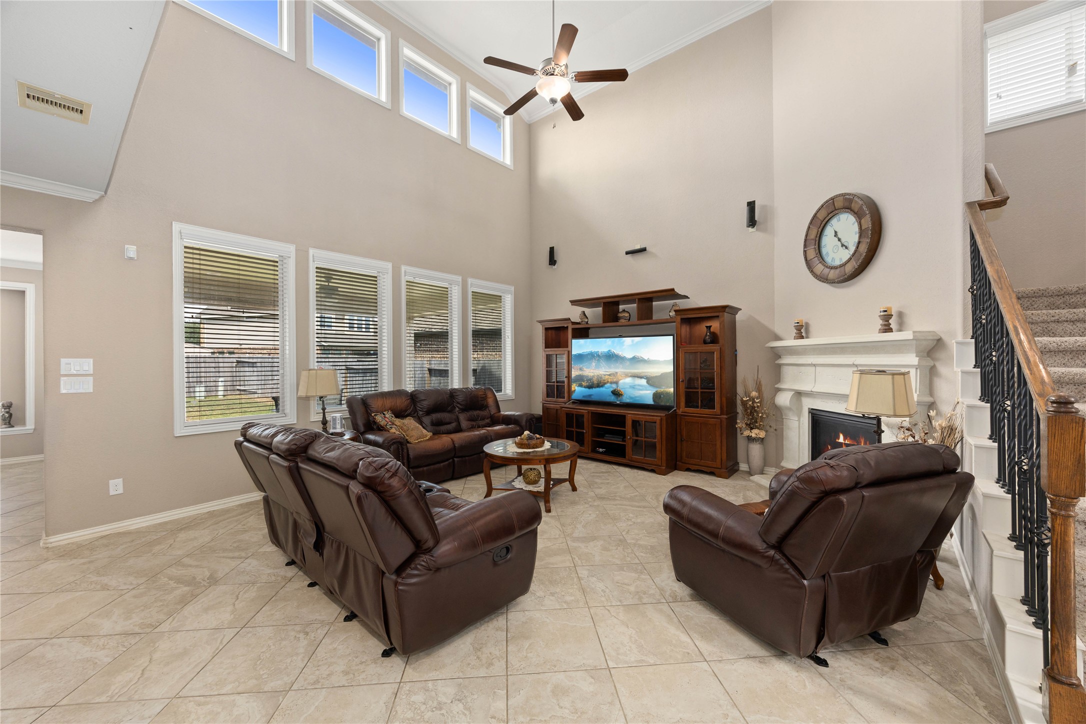 Spacious living room featuring high ceilings, abundant natural light from multiple windows, elegant tile flooring, and a cozy fireplace, perfect for relaxation and entertainment.