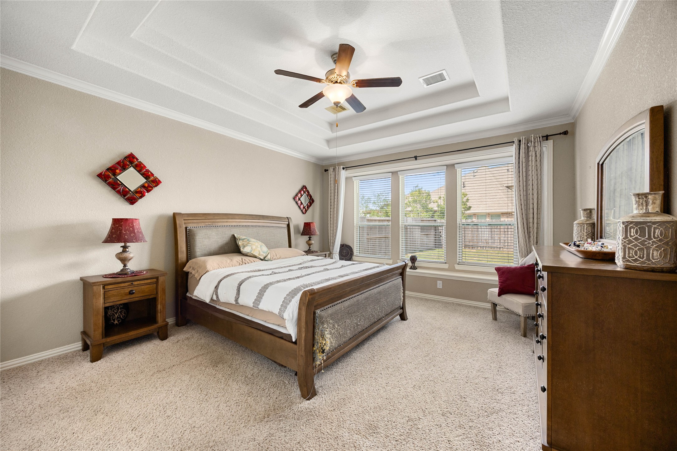 Spacious bedroom featuring a tray ceiling, elegant ceiling fan, and abundant natural light from large windows overlooking the backyard.