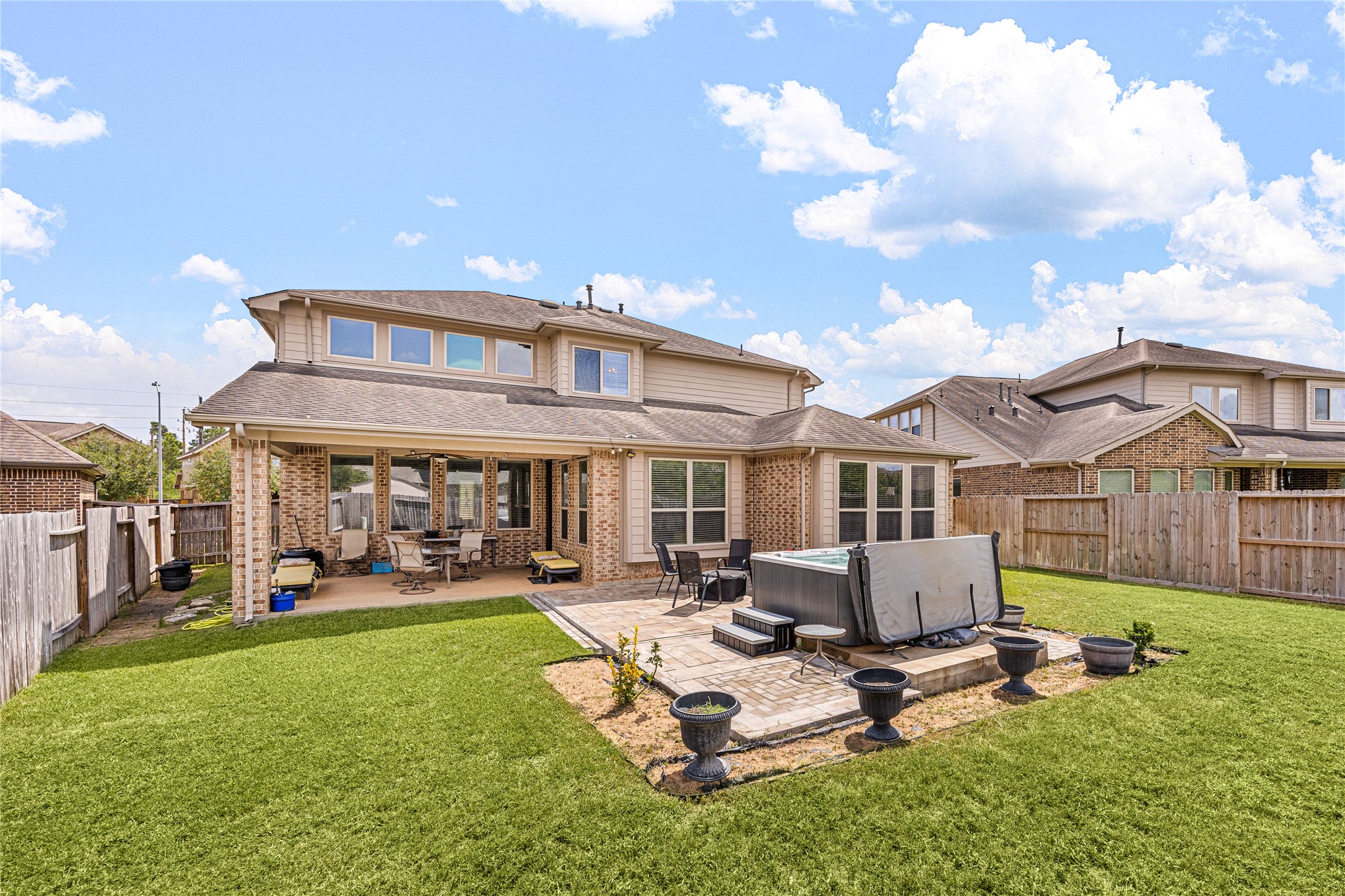 Spacious backyard featuring a covered patio and a luxurious hot tub, perfect for relaxation and entertaining.