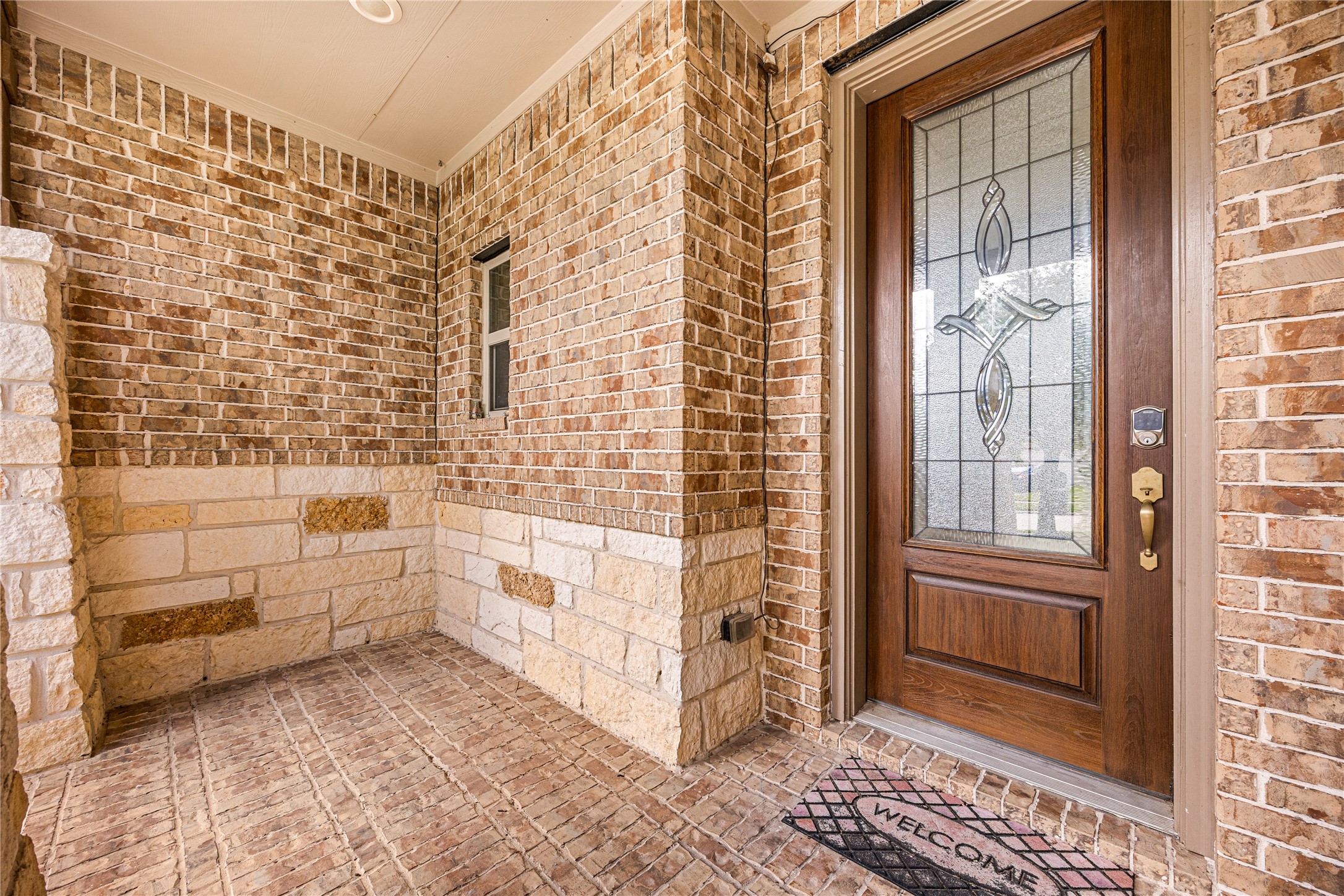 Charming entryway with elegant brickwork and a stylish wooden door featuring decorative glass, offering a warm welcome.