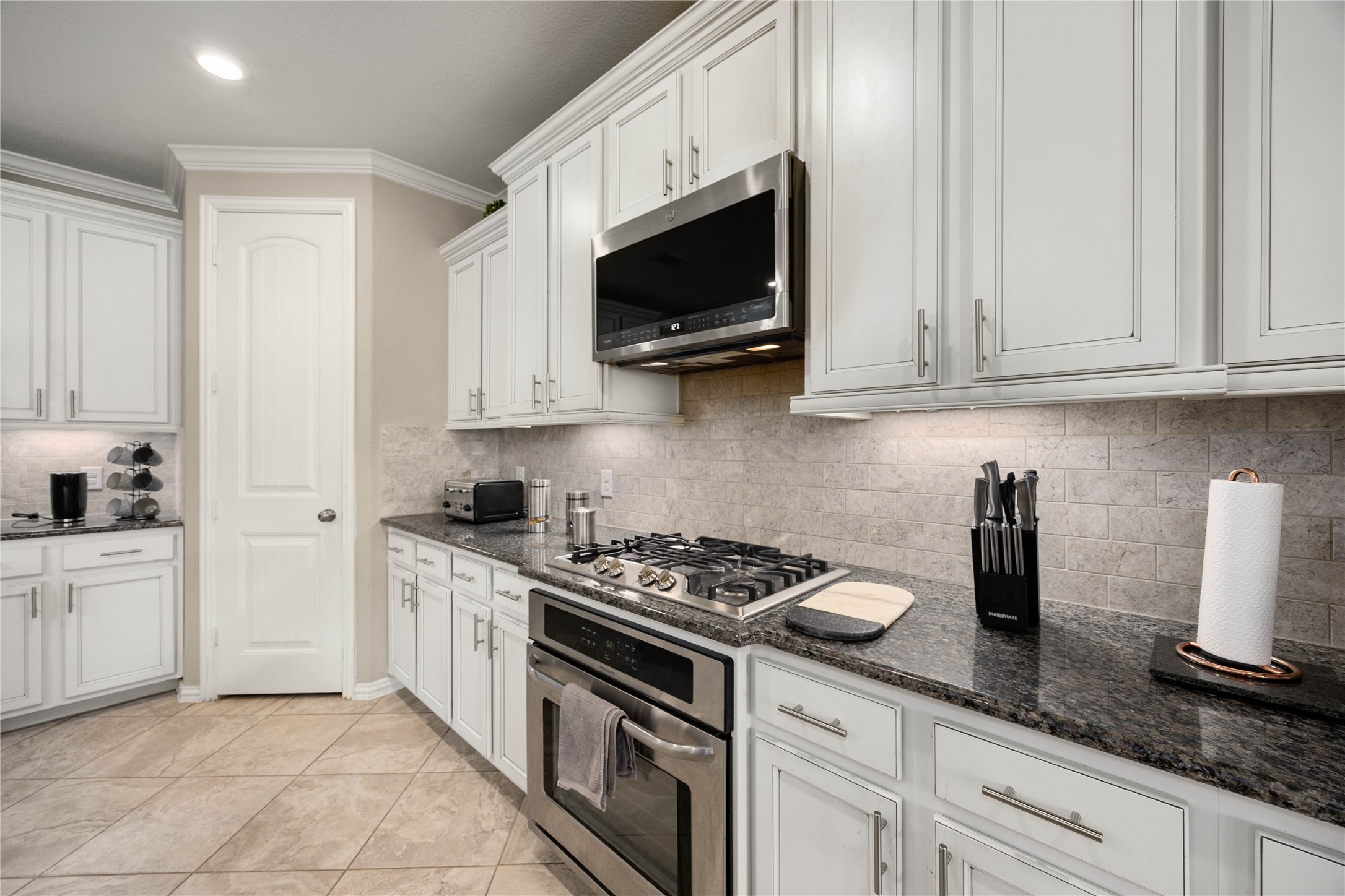 Sleek kitchen with modern stainless steel appliances, elegant white cabinetry, and granite countertops, enhanced by a stylish subway tile backsplash.