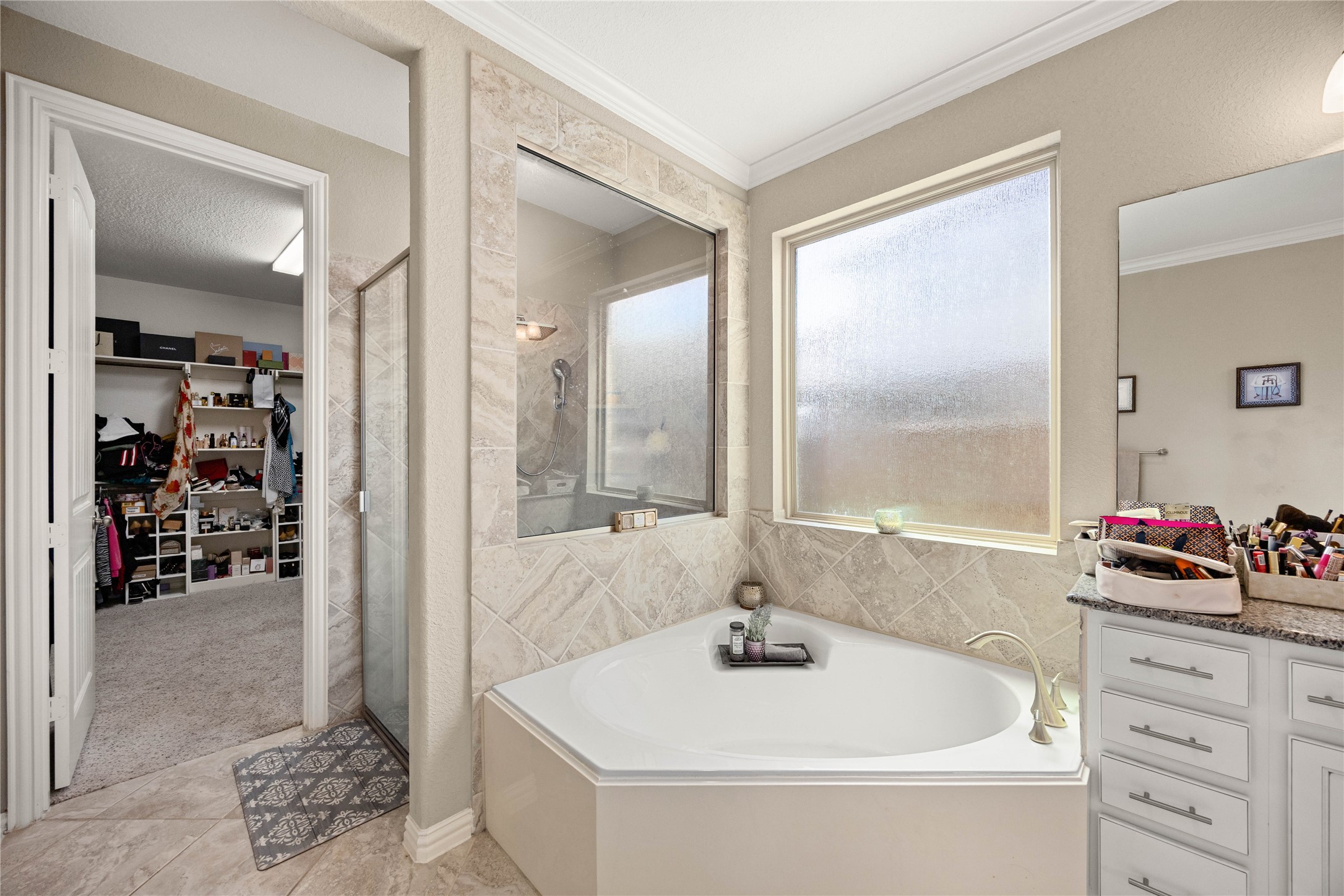 Luxurious bathroom featuring a spacious corner tub, sleek glass-enclosed shower, and ample natural light from frosted windows, seamlessly connected to a large walk-in closet.