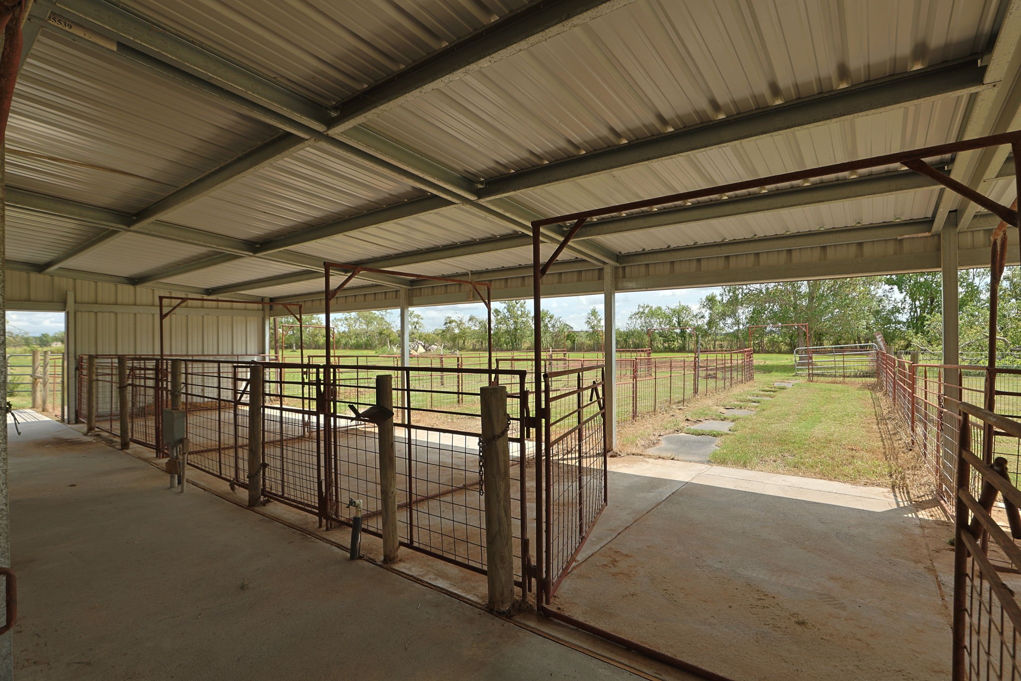 Spacious covered livestock area with sturdy metal fencing, offering easy access to open pastures and a secure environment for animals.