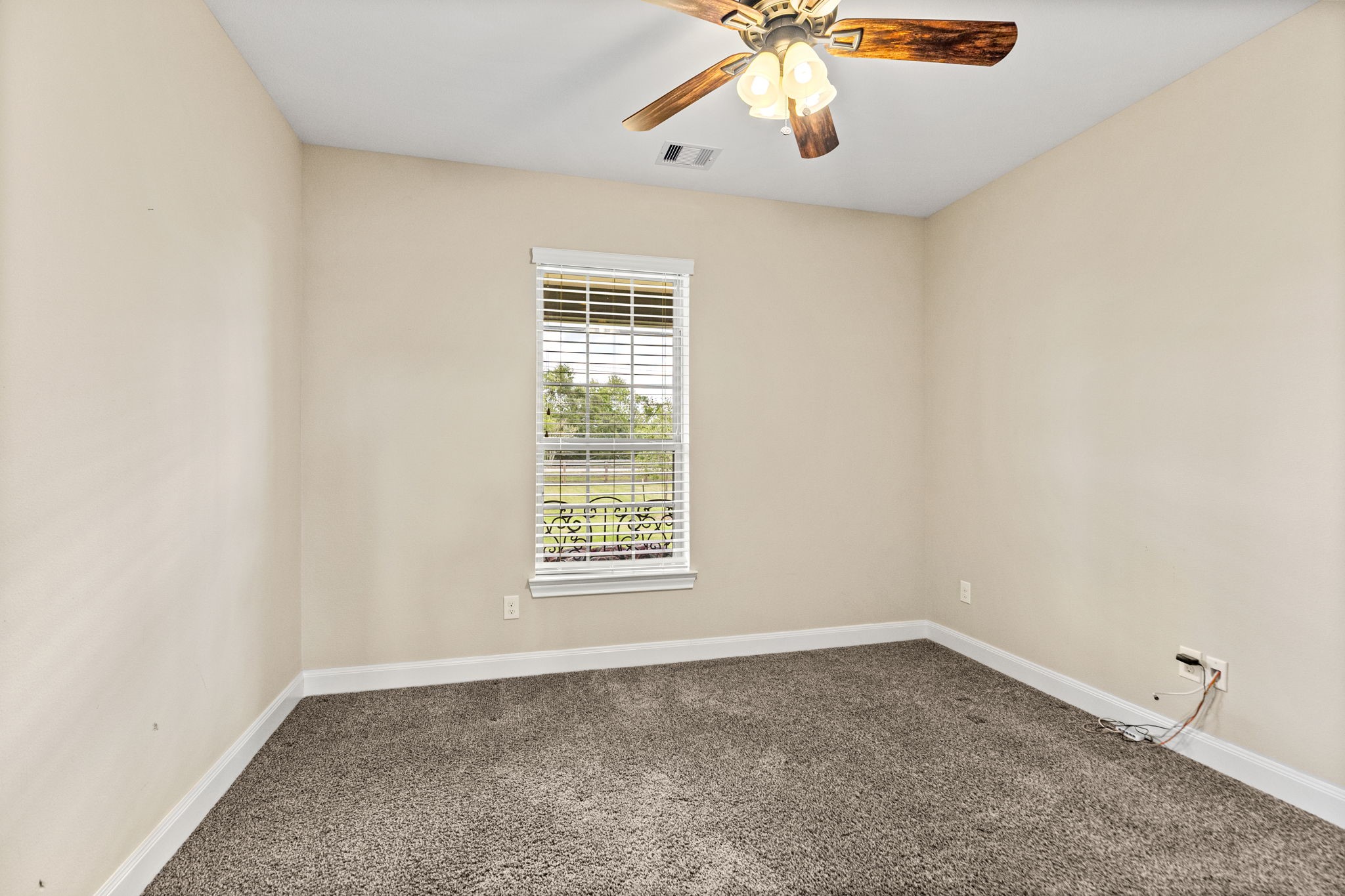 Cozy room with soft carpet flooring, a ceiling fan with lights, and a window offering a pleasant outdoor view.