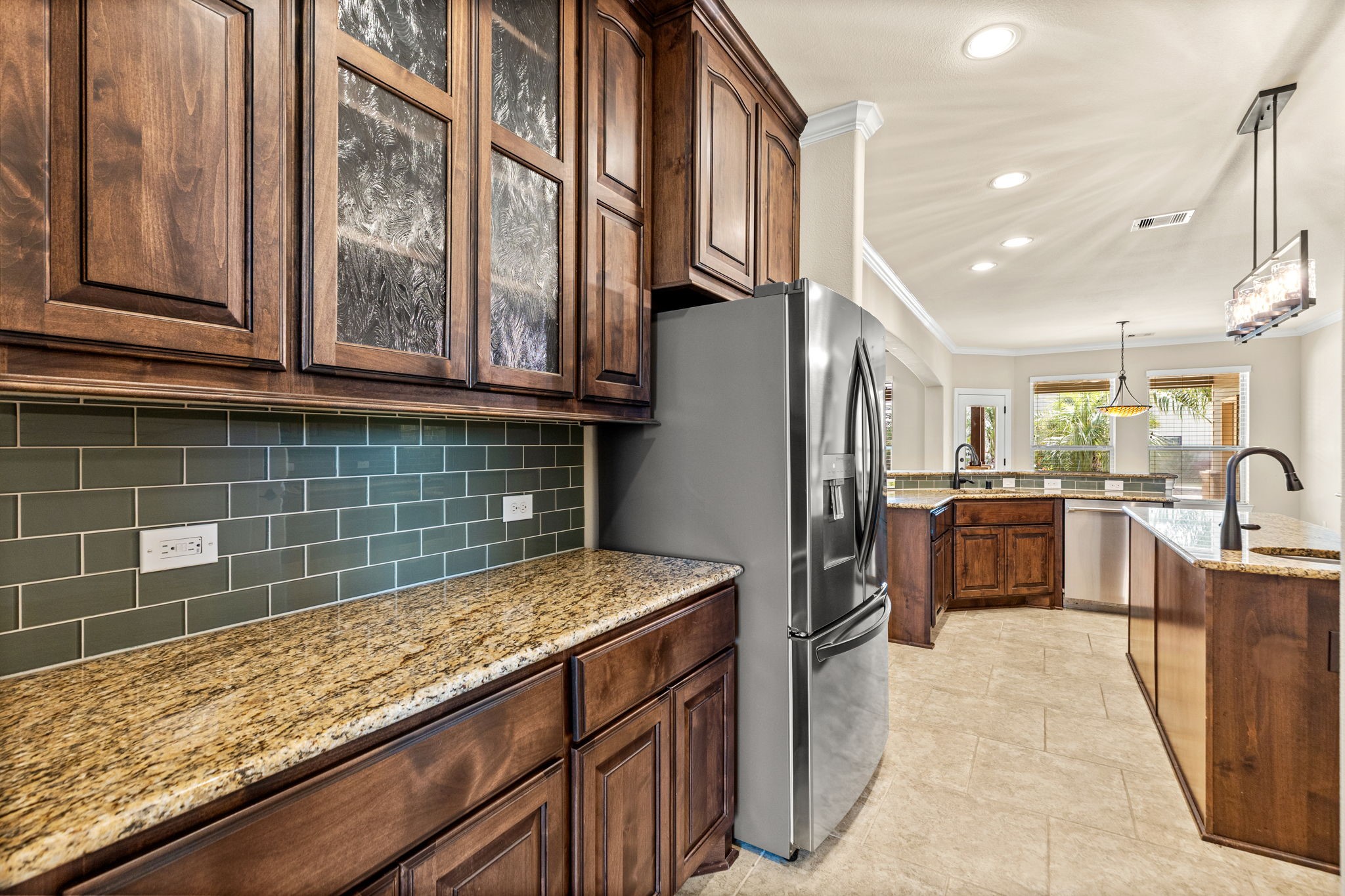 Spacious kitchen featuring elegant wooden cabinetry, sleek granite countertops, and a modern stainless steel refrigerator, complemented by a stylish tile backsplash and ample natural light.