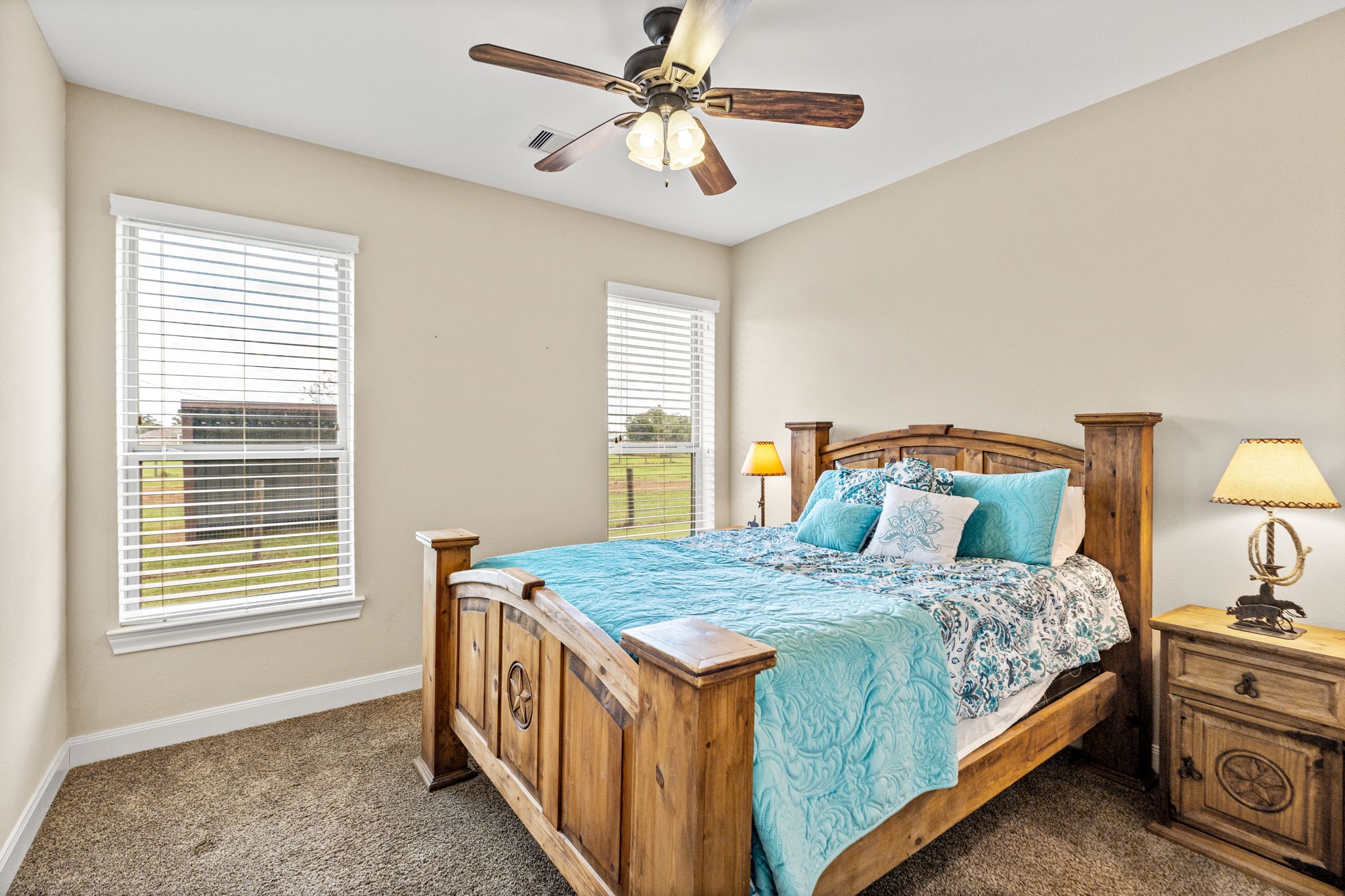 Cozy bedroom featuring a rustic wooden bed, plush carpeting, and abundant natural light from two large windows.