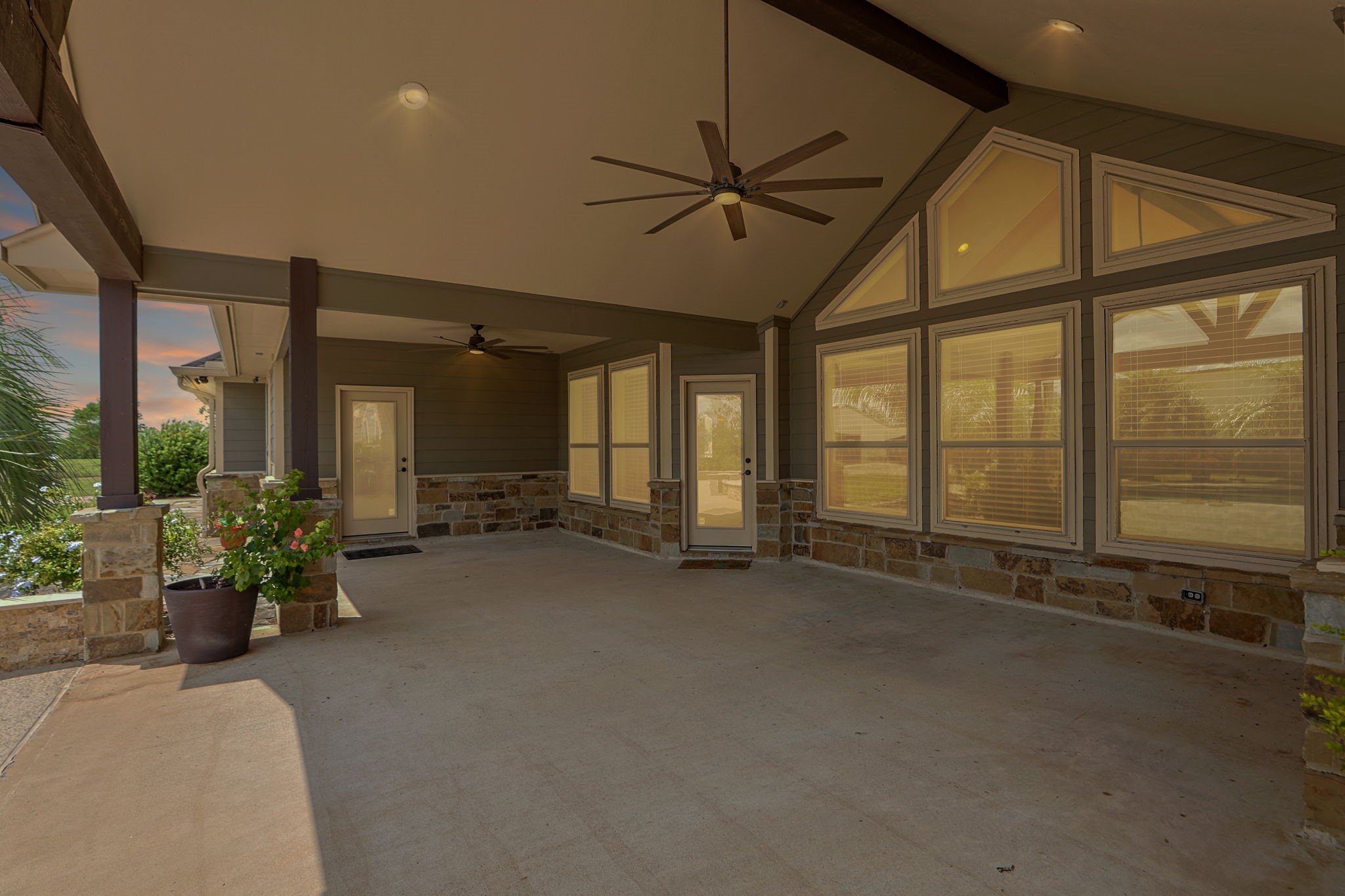 Spacious covered patio with vaulted ceiling, fans, and large windows, perfect for outdoor relaxation and entertaining.