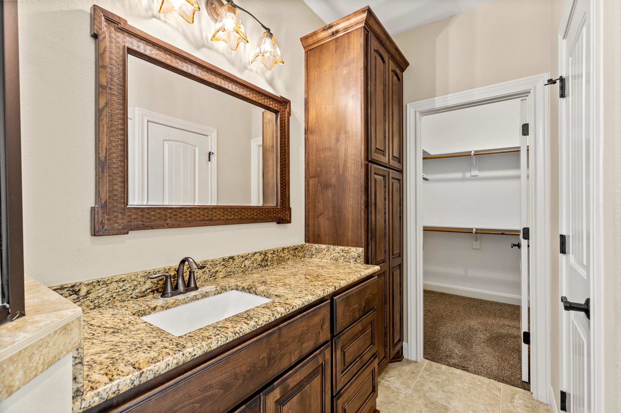 Elegant bathroom with rich wood cabinetry and granite countertops, leading to a spacious walk-in closet.