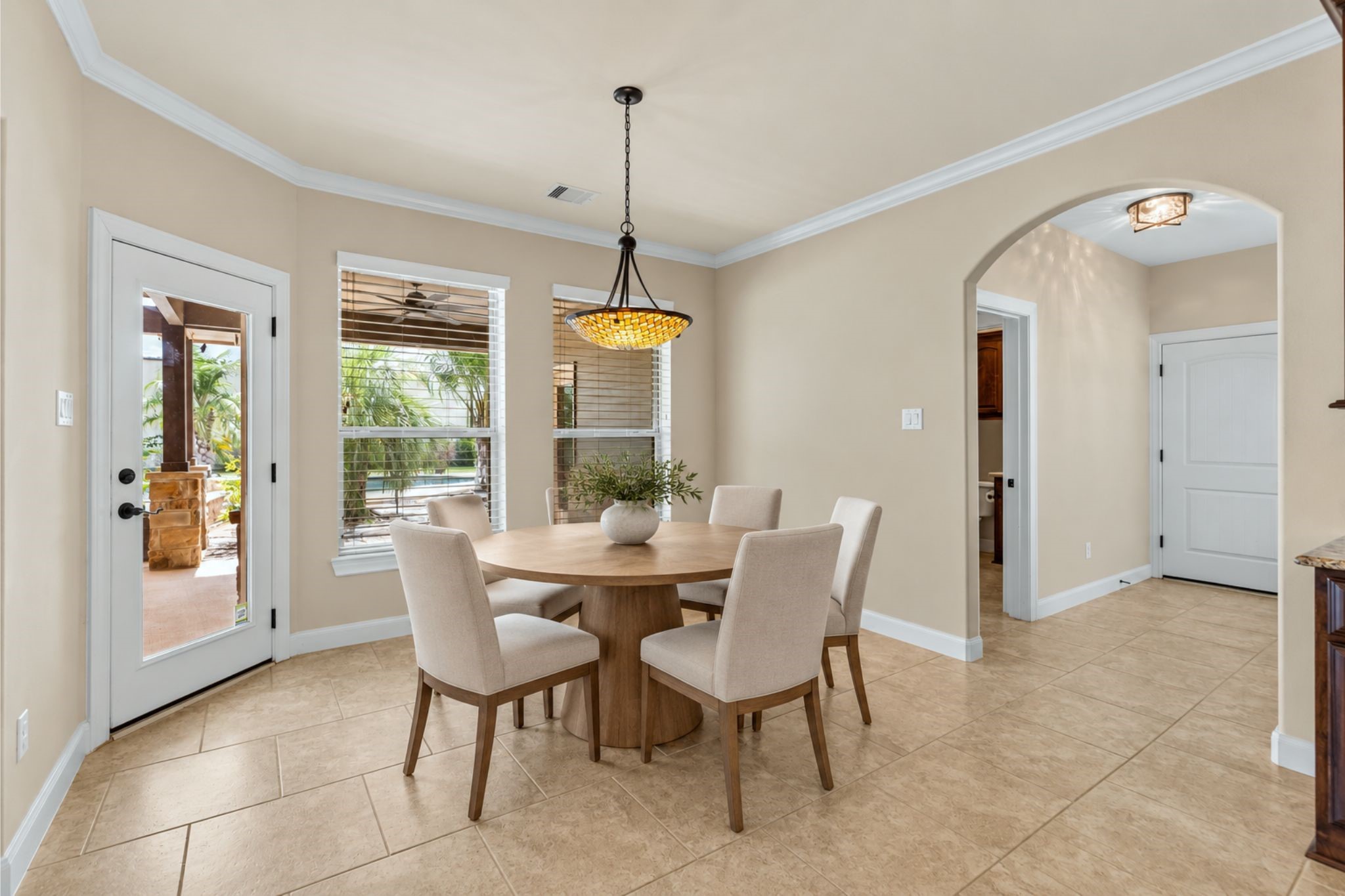 Bright dining area with elegant tile flooring, a stylish round table, and chairs. The space features a large window and glass door leading to an inviting outdoor patio.  **VIRTUAL STAGING, DECOR ONLY HAS BEEN ADDED**
