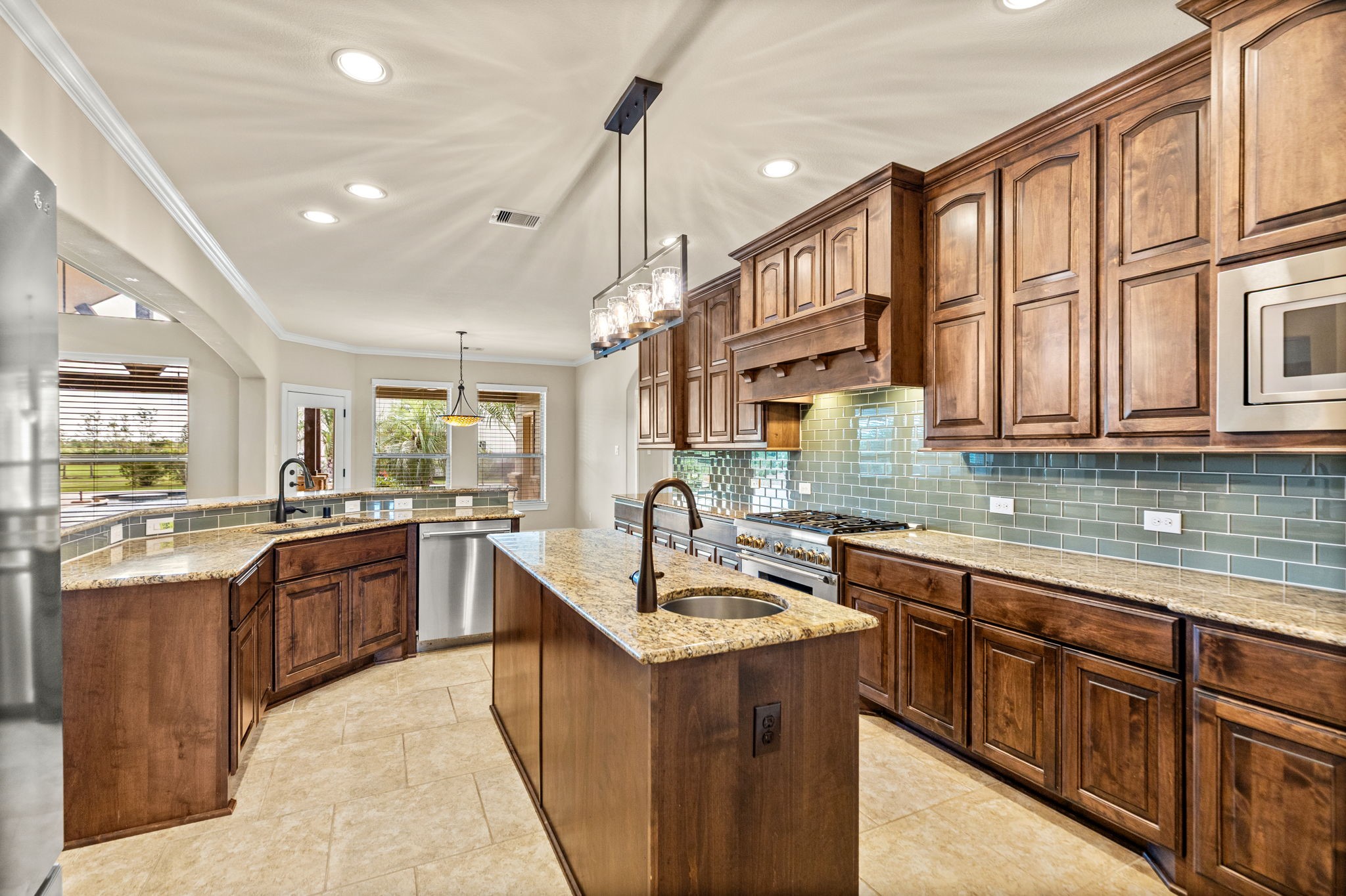 Spacious kitchen with rich wooden cabinetry, granite countertops, and a central island, complemented by stainless steel appliances and elegant tile backsplash.