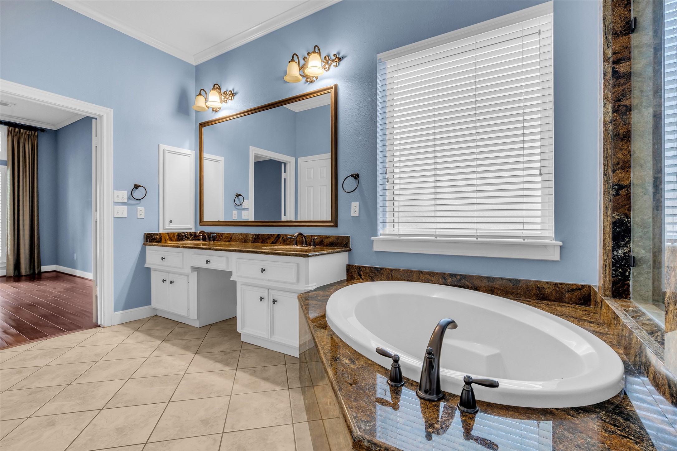 Spacious primary bathroom with granite countertops, soaking tub, separate glass-enclosed shower, two walk-in-closets