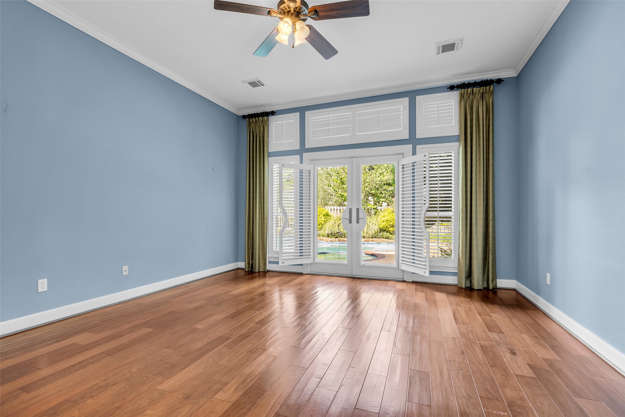 Spacious first-floor primary bedroom with hardwood floors, high ceilings, and French doors overlooking the private pool.