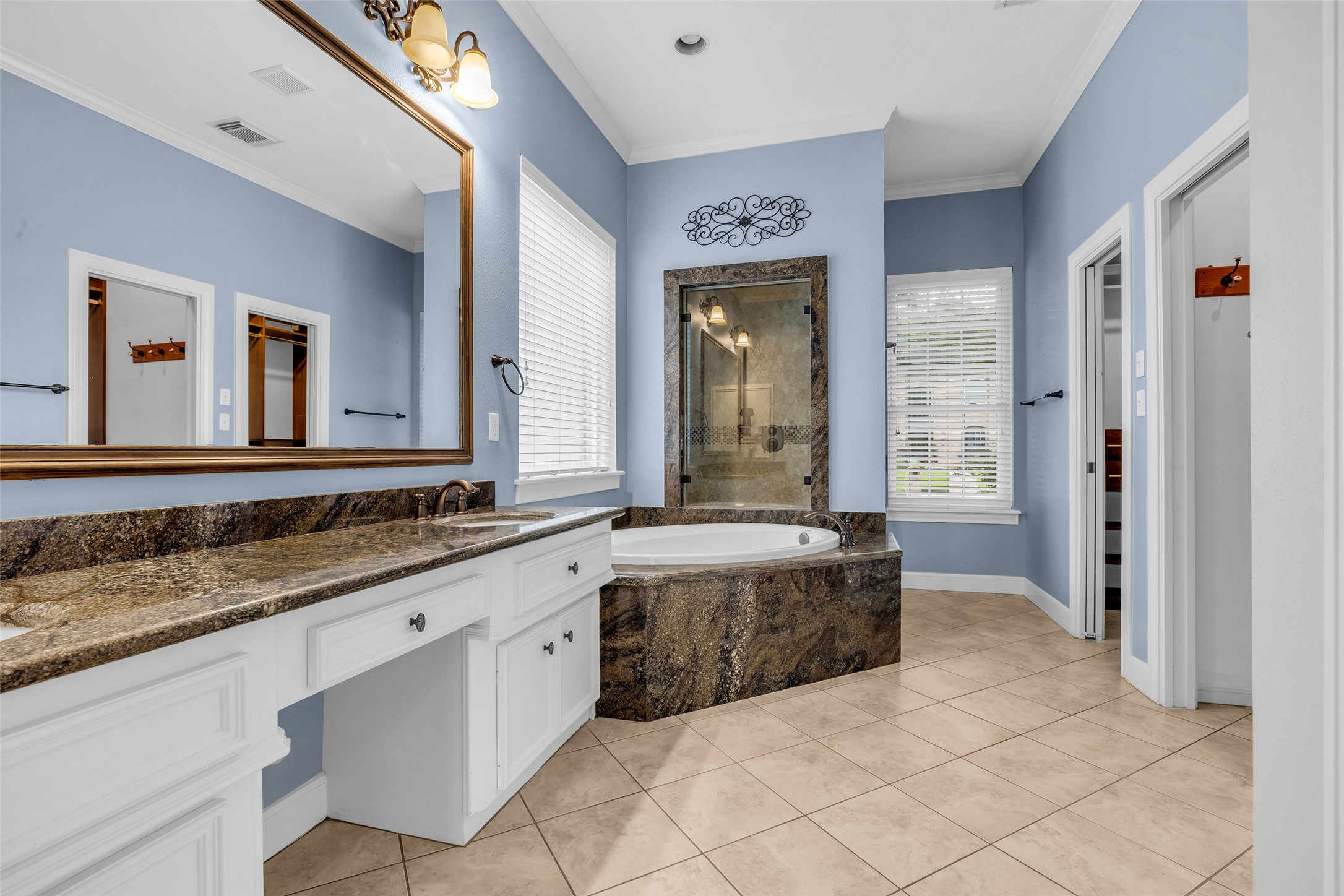 Spacious primary bathroom with granite countertops, soaking tub, separate glass-enclosed shower, two walk-in-closets