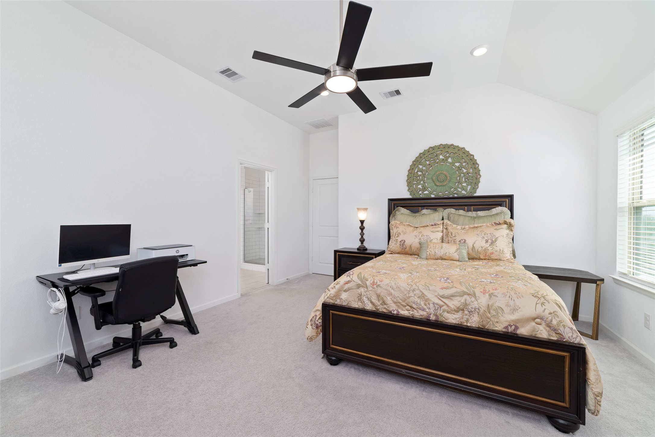The spacious primary bedroom features plush carpeting, a ceiling fan, neutral walls, and ample room for a king-sized bed and additional furnishings.