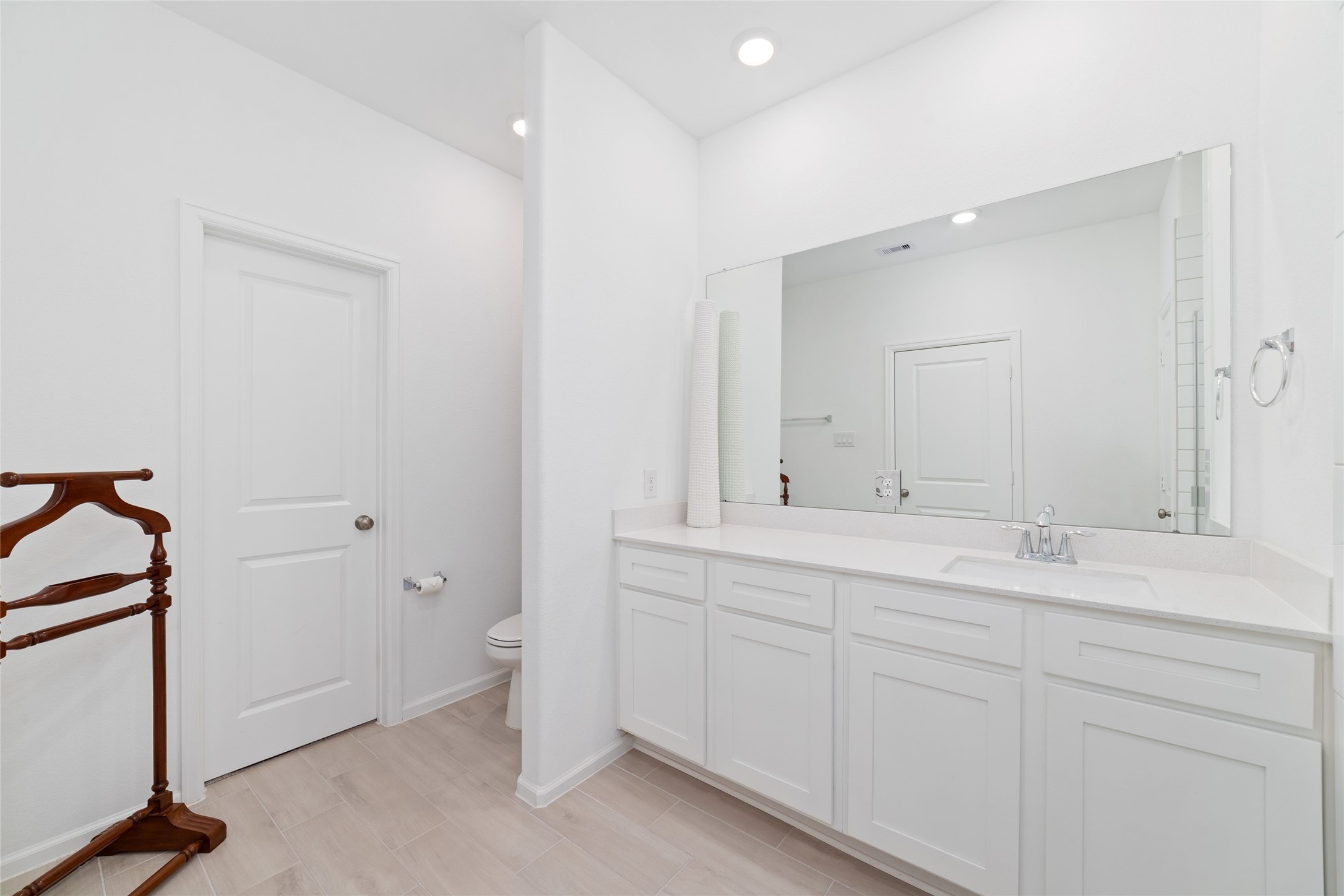 Another view of the primary bathroom highlights the vanity area, neutral finishes, and convenient layout.