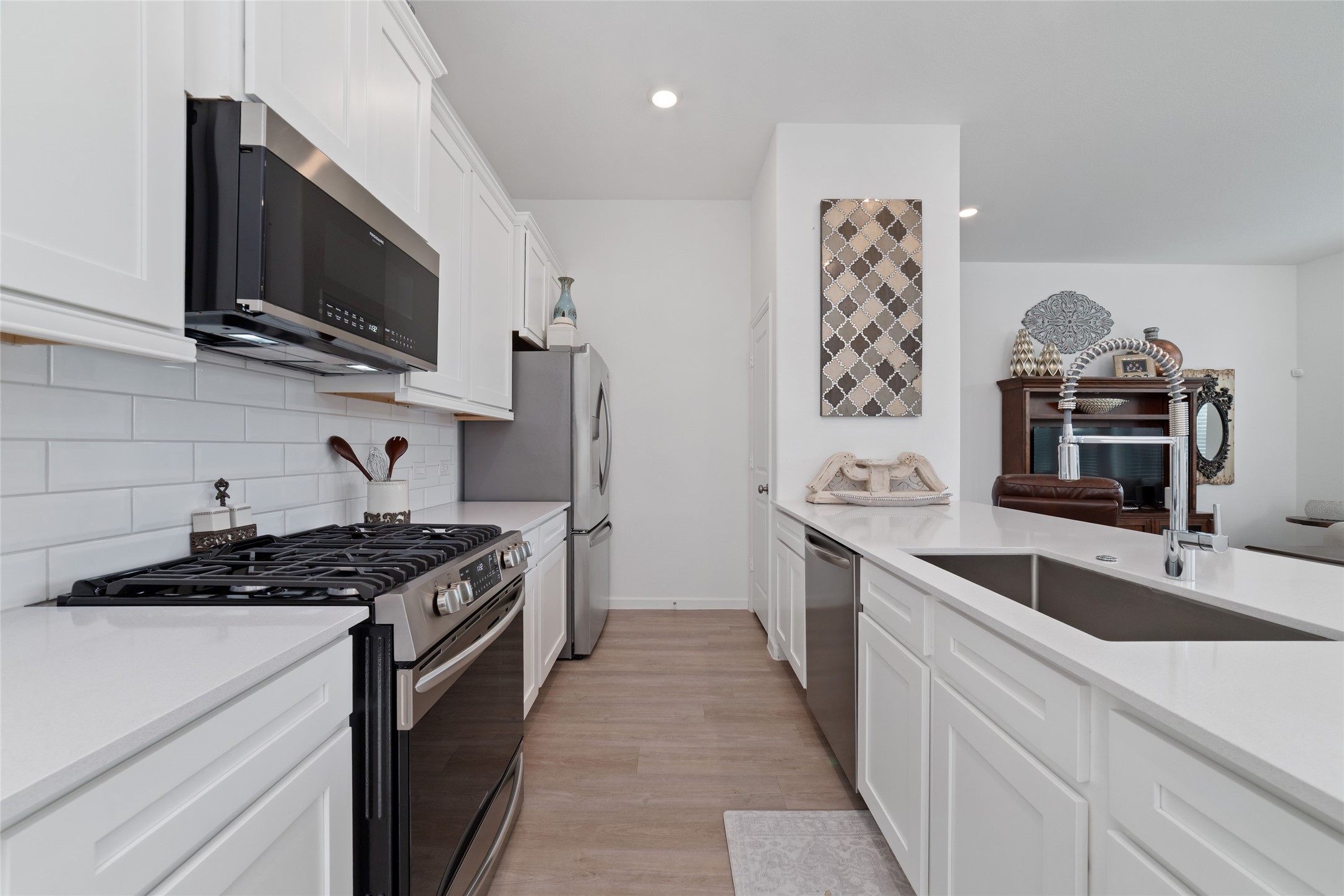 The kitchen features crisp white cabinetry, a gas range, built-in microwave, dishwasher, generous counter space, and a functional layout for meal preparation.