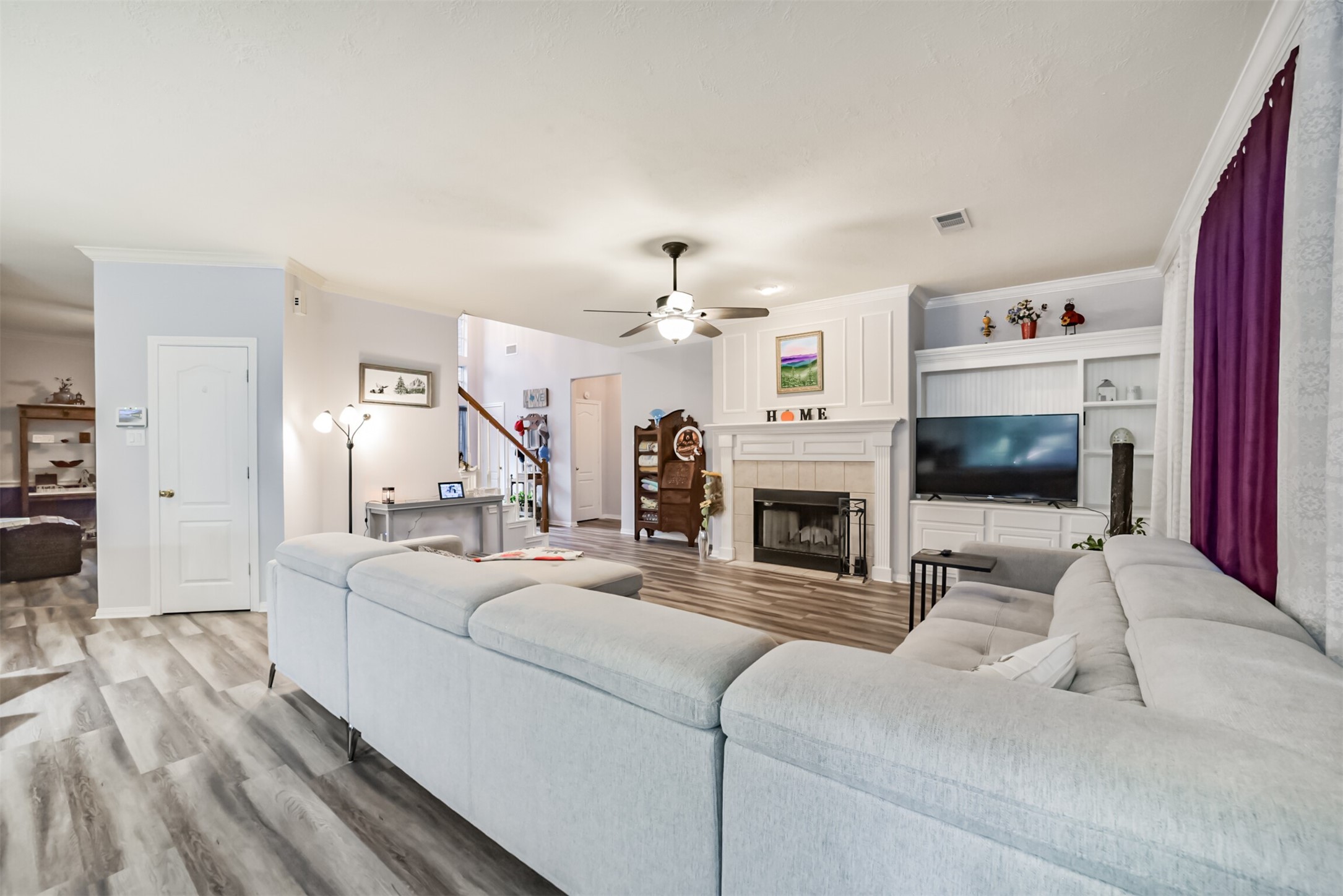 A view of the family room from the breakfast room, featuring a tile-accented fireplace with a wood mantel and built-in cabinets with display shelves.