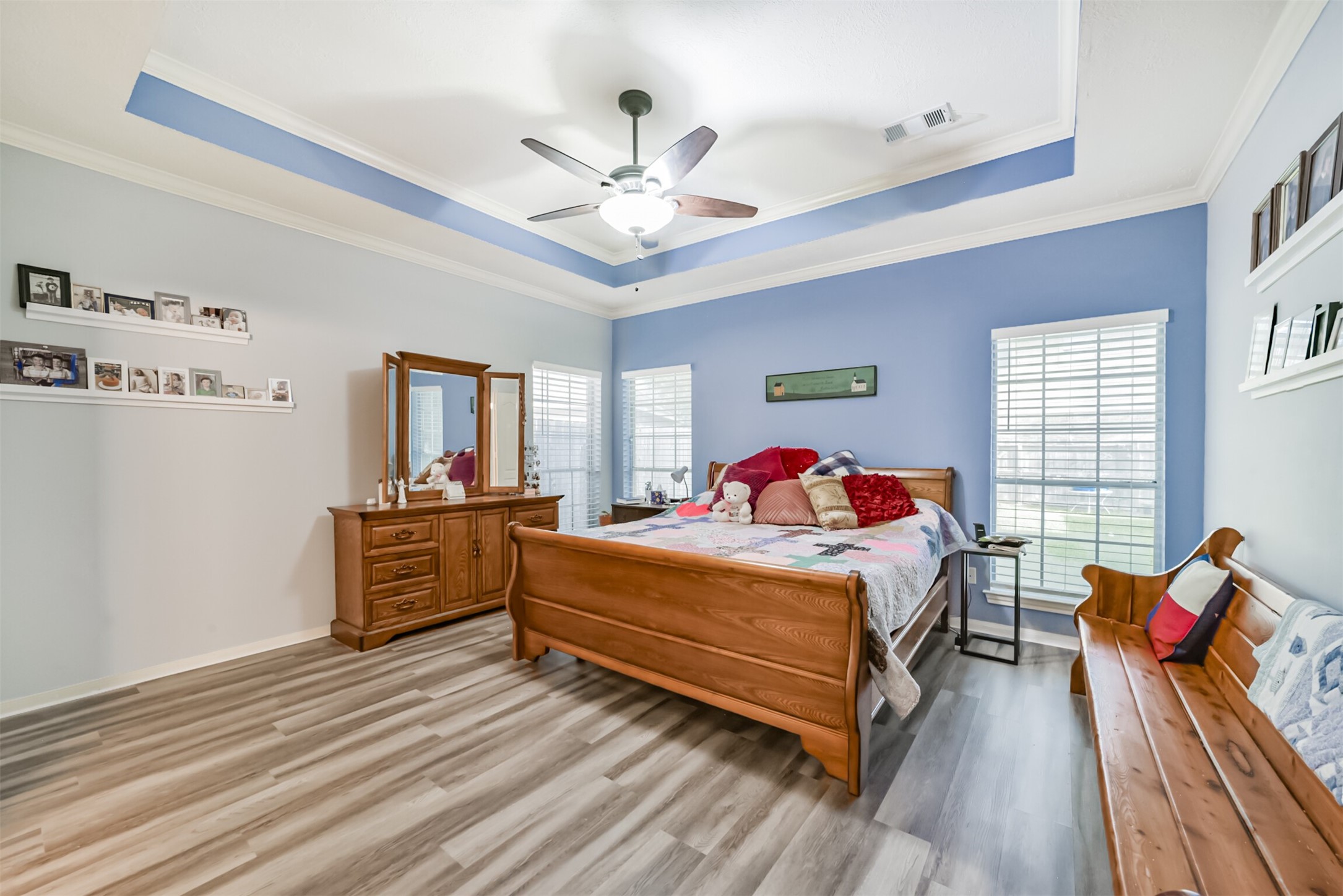 The primary bedroom is located on the first floor and features a double coffered ceiling with a ceiling fan and light fixture. Three sets of windows bring ambient lighting to the bedroom.