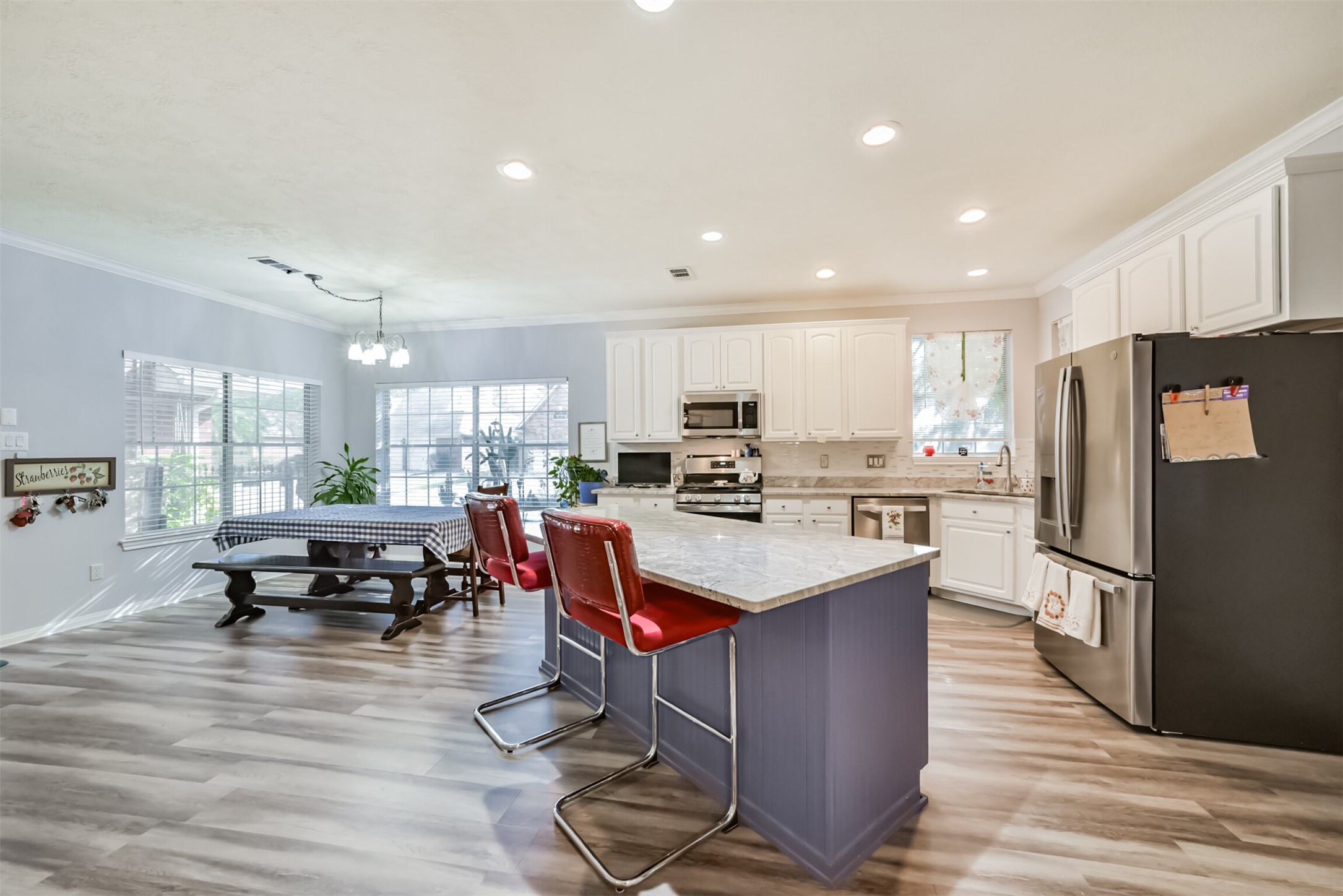 A center island anchors the kitchen, complemented by a sunlit breakfast room with two corner windows. Crown molding, tall cabinets, and stainless steel appliances complete the space.