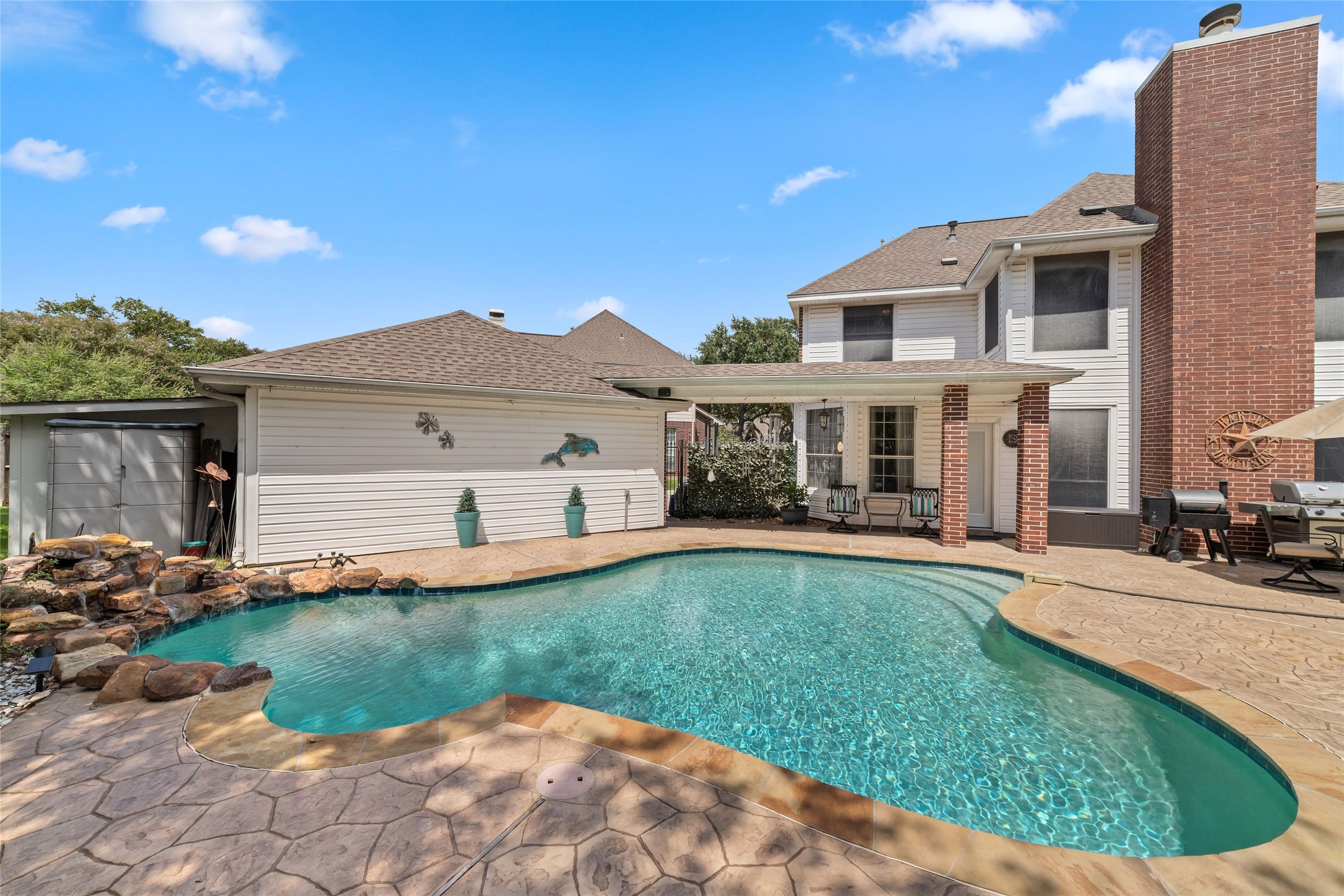 Poolside view highlighting the water feature, mature landscaping, and surrounding patio space.