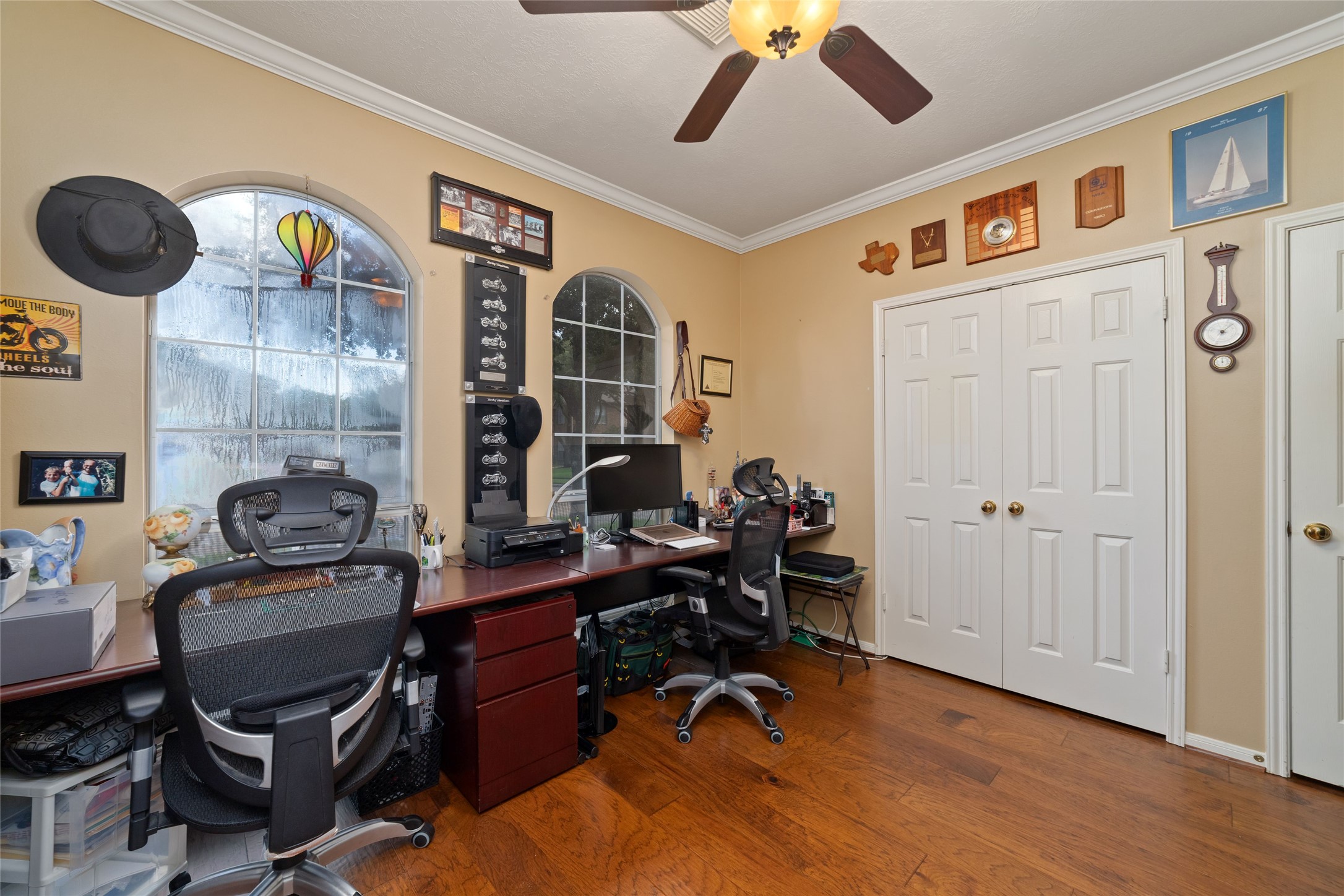 Dedicated home office with arched windows, crown molding, ceiling fan, and double-door closet.