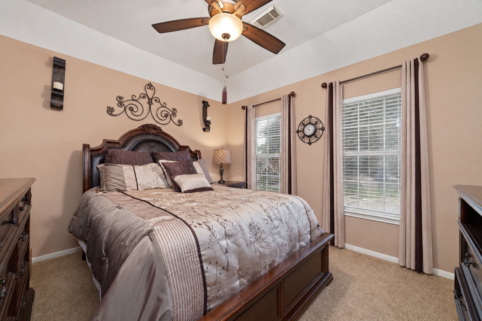 Upstairs bedroom with tray ceiling, ceiling fan, carpet, and two windows overlooking the property.