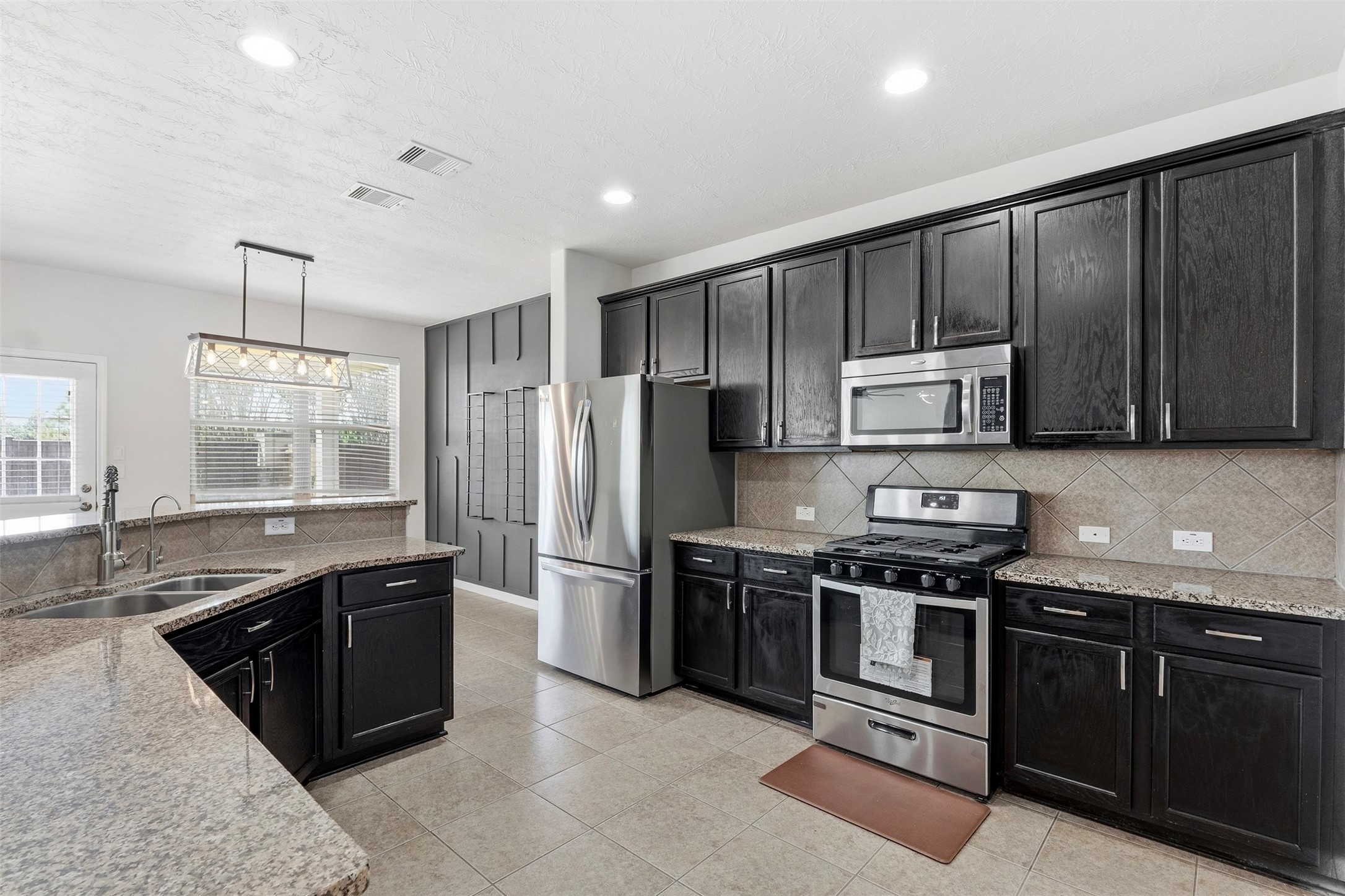 Spacious kitchen featuring dark wood cabinetry, granite countertops, tile flooring, and modern stainless steel appliances.