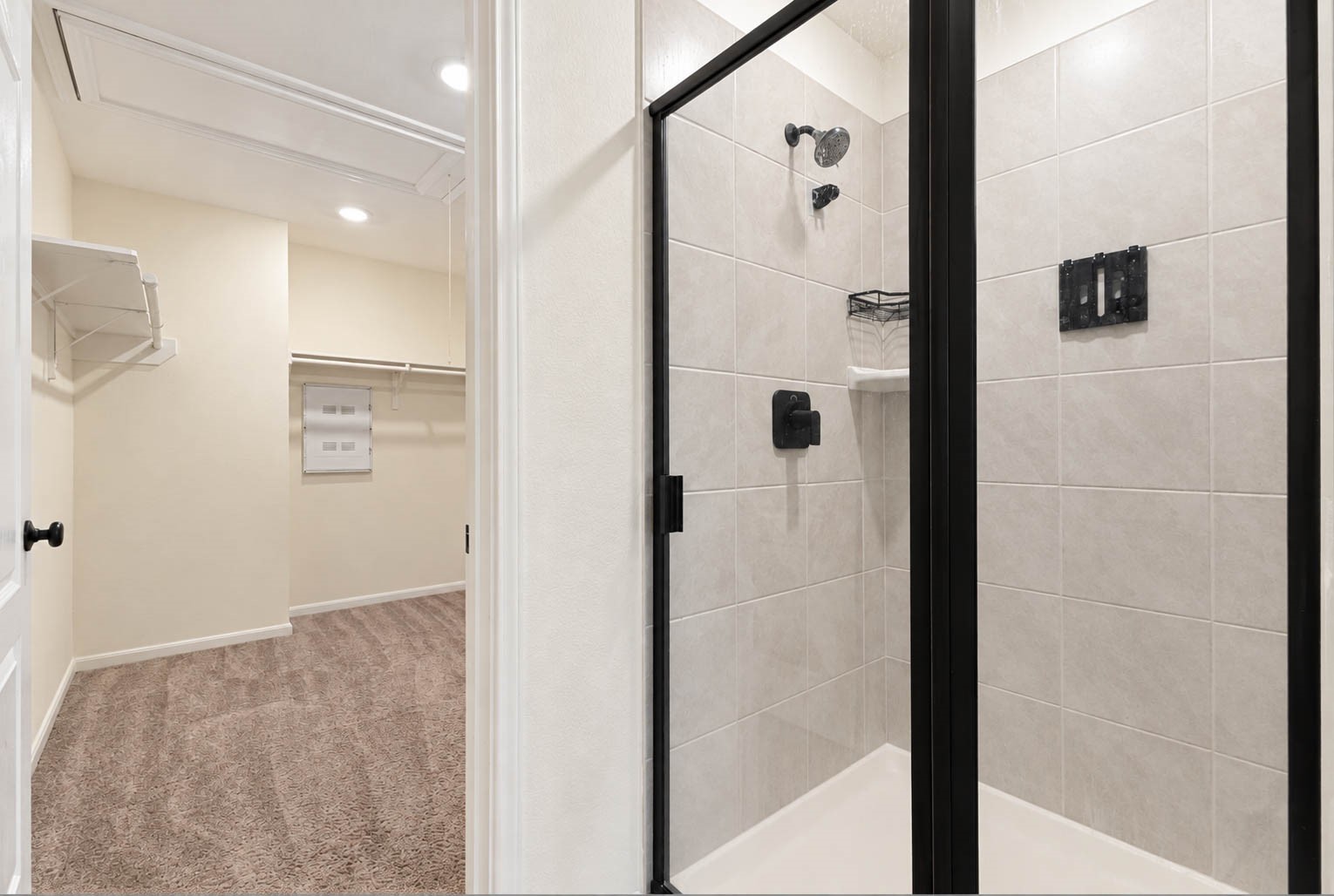 The spacious walk-in shower showcases beautiful coordinating tilework, a sleek black-framed glass enclosure, & convenient corner shelving, adding both style & functionality to the primary bath.