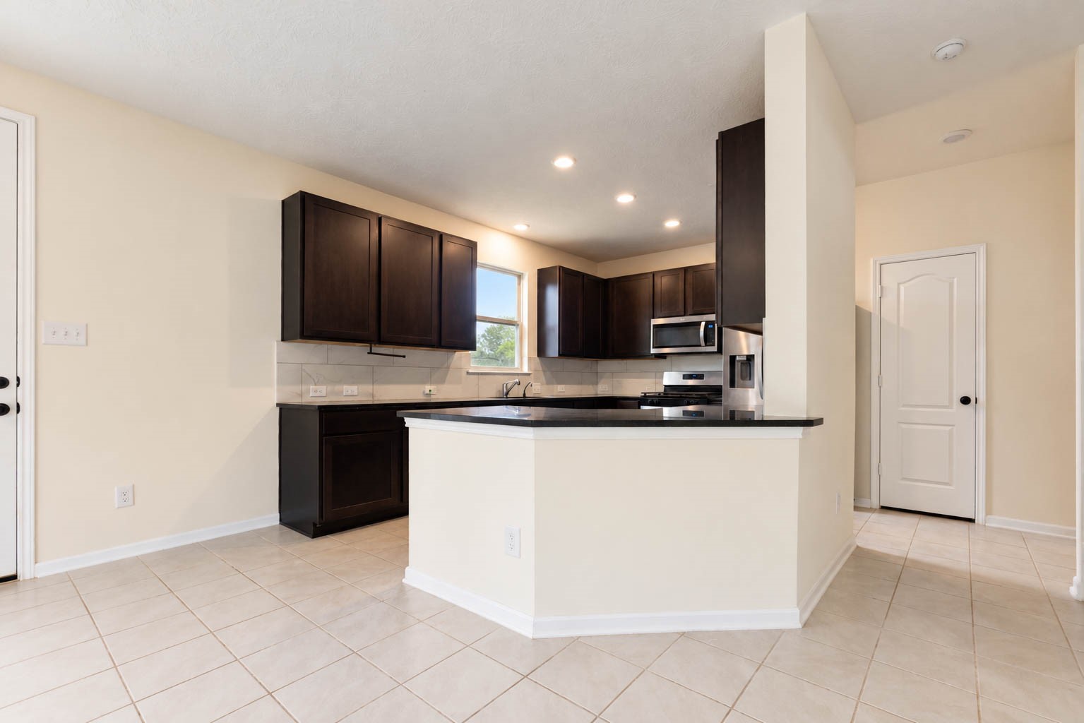 Rich espresso-toned cabinetry brings warmth & sophistication to the kitchen, while a spacious breakfast bar provides additional seating for casual dining. A nearby door offers convenient access to the covered patio & backyard, creating an effortless transition to outdoor living.