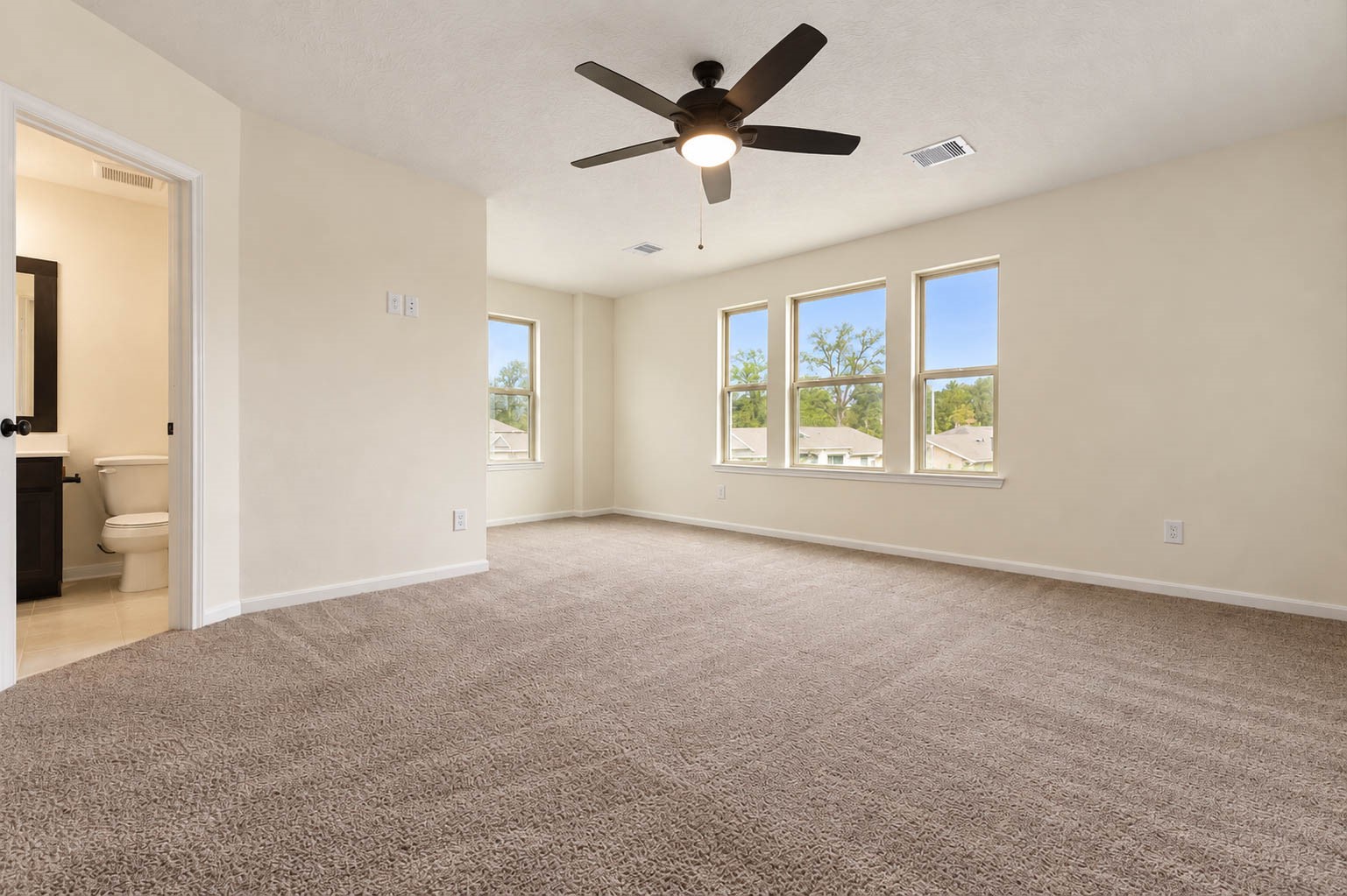 Plush carpeting, a soothing neutral color palette, & a stylish ceiling fan enhance the room's warmth & comfort, while multiple windows fill the space with abundant natural light, creating a bright & relaxing retreat.