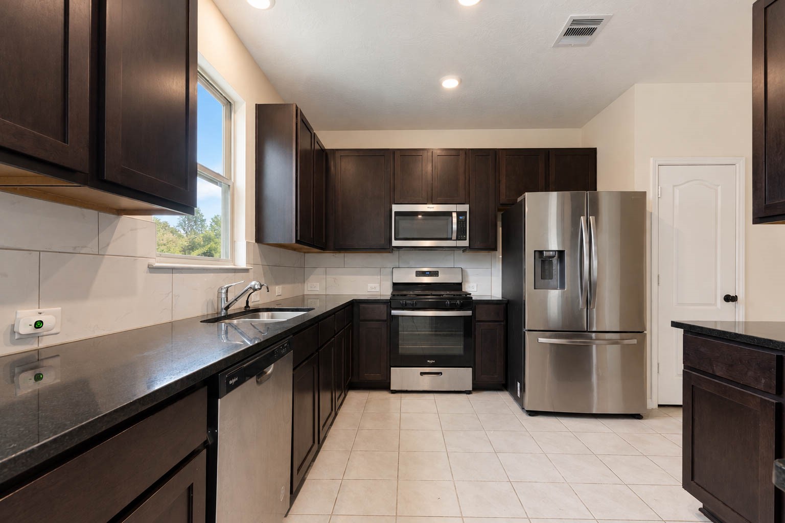 The beautifully appointed kitchen showcases sleek granite countertops, a stylish tile backsplash, & abundant cabinetry, complemented by generous counter space & a convenient pantry for exceptional storage & everyday functionality.