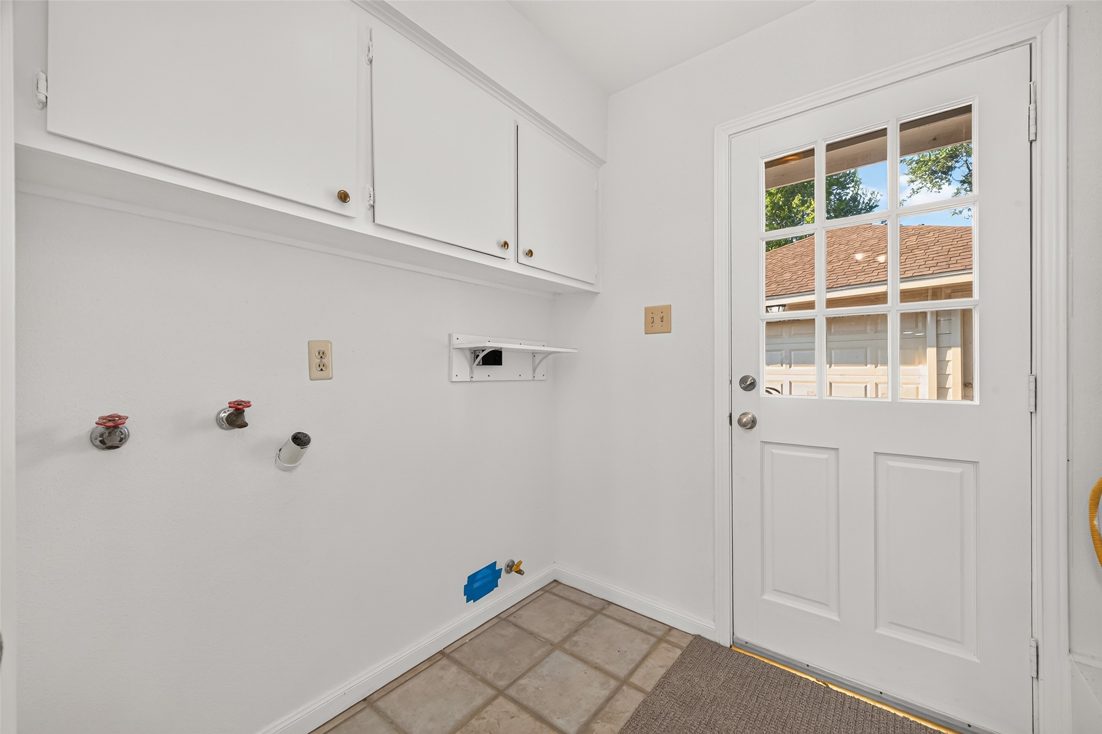 Conveniently located laundry room featuring washer and dryer connections, overhead cabinetry for additional storage, and easy-to-maintain tile flooring. A charming glass-paneled exterior door welcomes natural light and provides direct access to the driveway and detached garage.