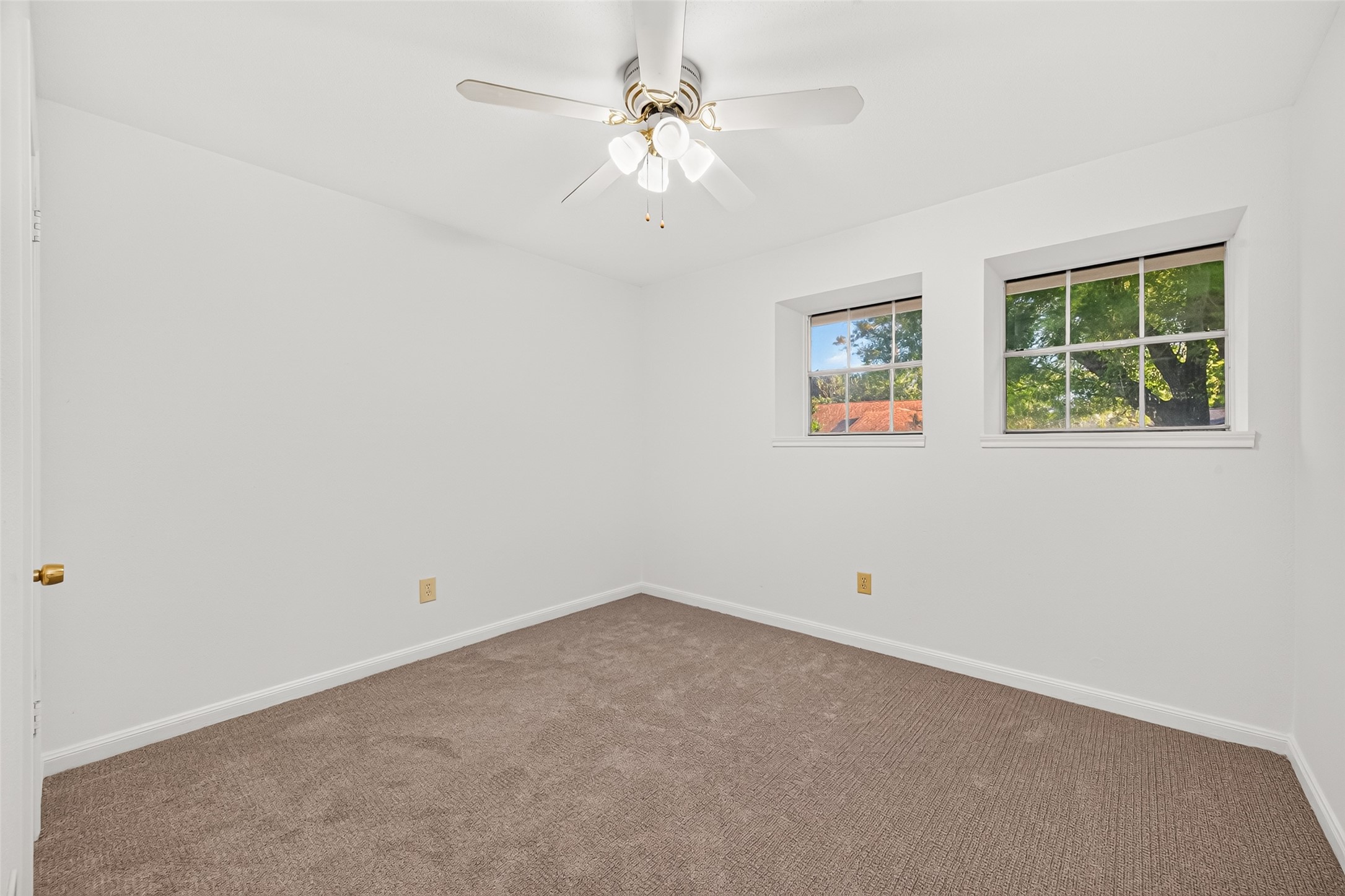 Bright and inviting secondary bedroom featuring two charming windows with deep windowsills that add architectural character while offering lovely views of the surrounding greenery. Fresh neutral paint, soft carpeting, and a ceiling fan create a welcoming atmosphere, while a spacious walk-in closet.