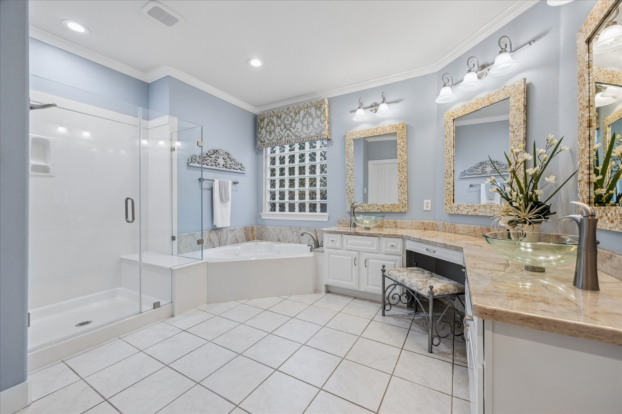 The primary bath offers a relaxing retreat with dual vanities, a jetted tub, and a frameless glass-enclosed shower, creating a comfortable space to unwind and recharge.
