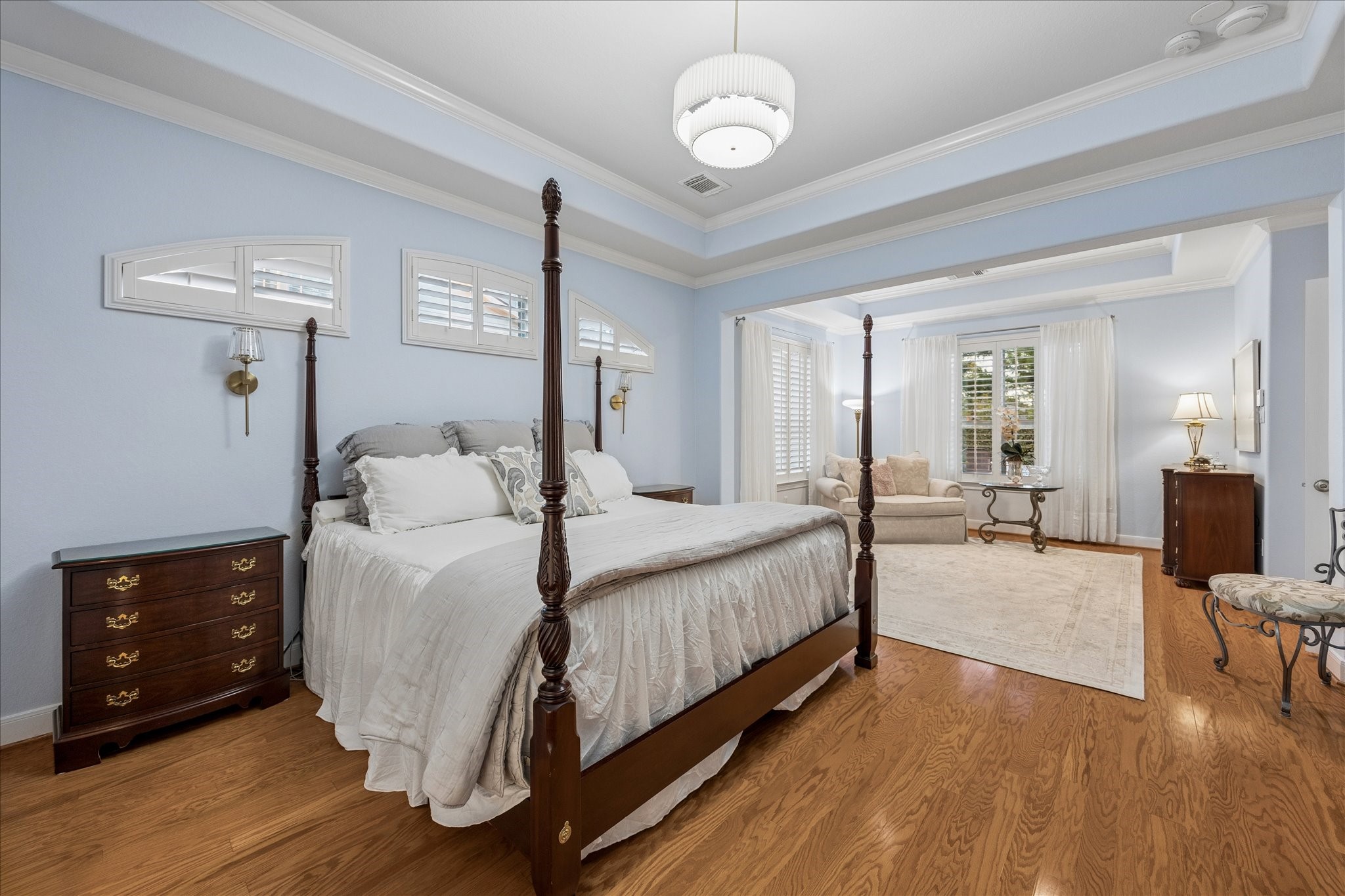 The secluded primary retreat offers a warm, inviting atmosphere with warm wood flooring, elegant tray ceilings, and refined crown molding.