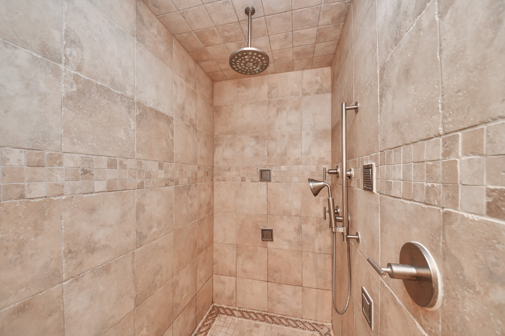 Walk-in shower features floor-to-ceiling tile, a rainfall showerhead, handheld sprayer and body sprays.