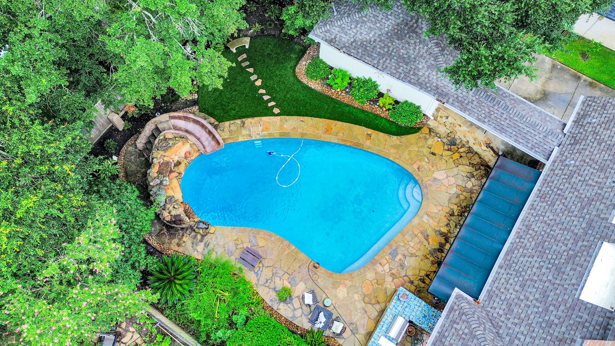 The oversized pool features a rock waterfall and slide, with mature landscaping creating a private backyard setting.