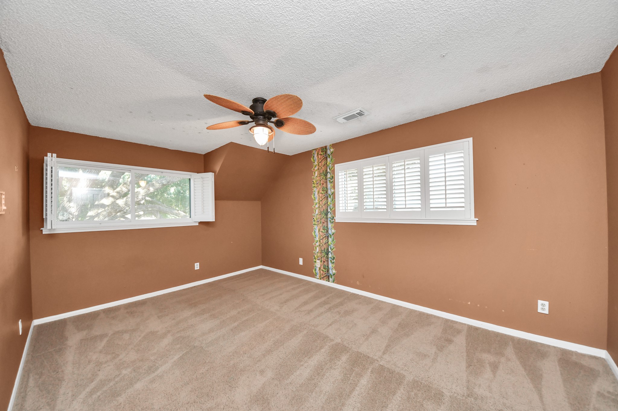 Multiple windows and plantation shutters bring natural light into this generously sized secondary bedroom.