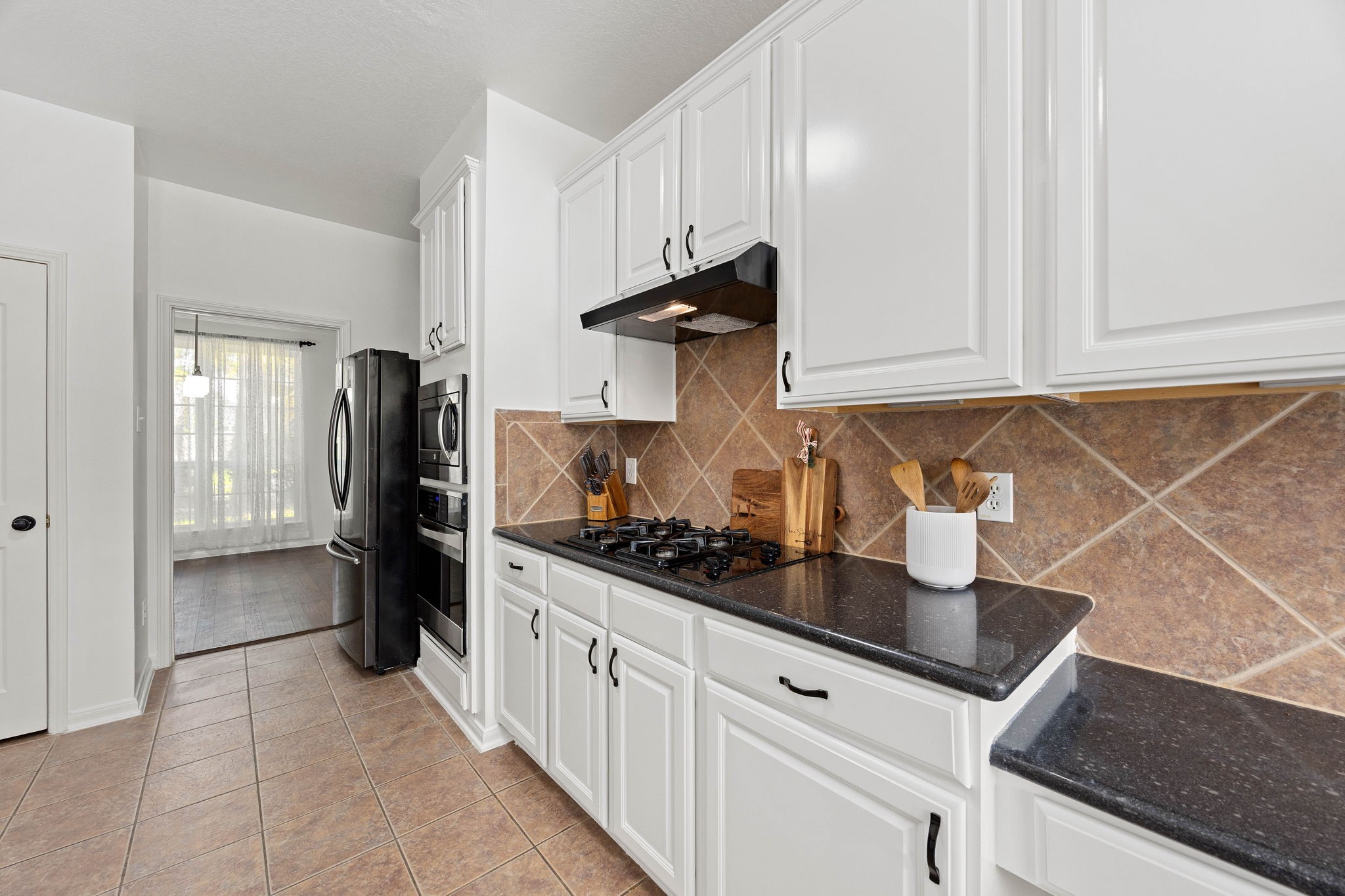 Kitchen view highlighting abundant white cabinetry, extensive countertop space, tile backsplash, and appliance area.