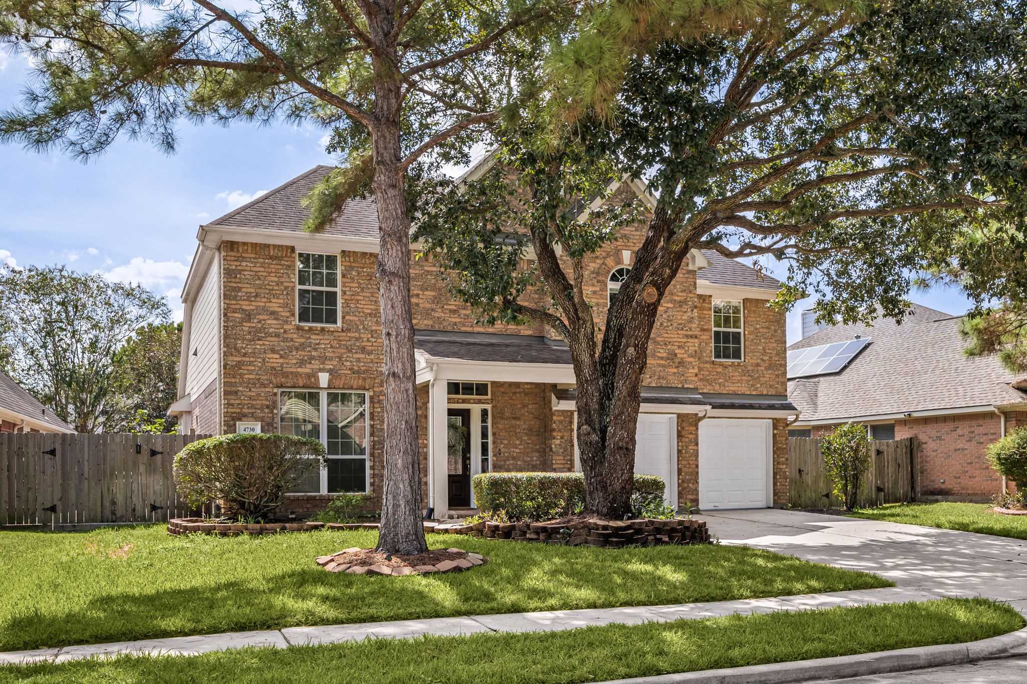 Front exterior view highlighting the mature landscaping, spacious driveway, and attached two-car garage.