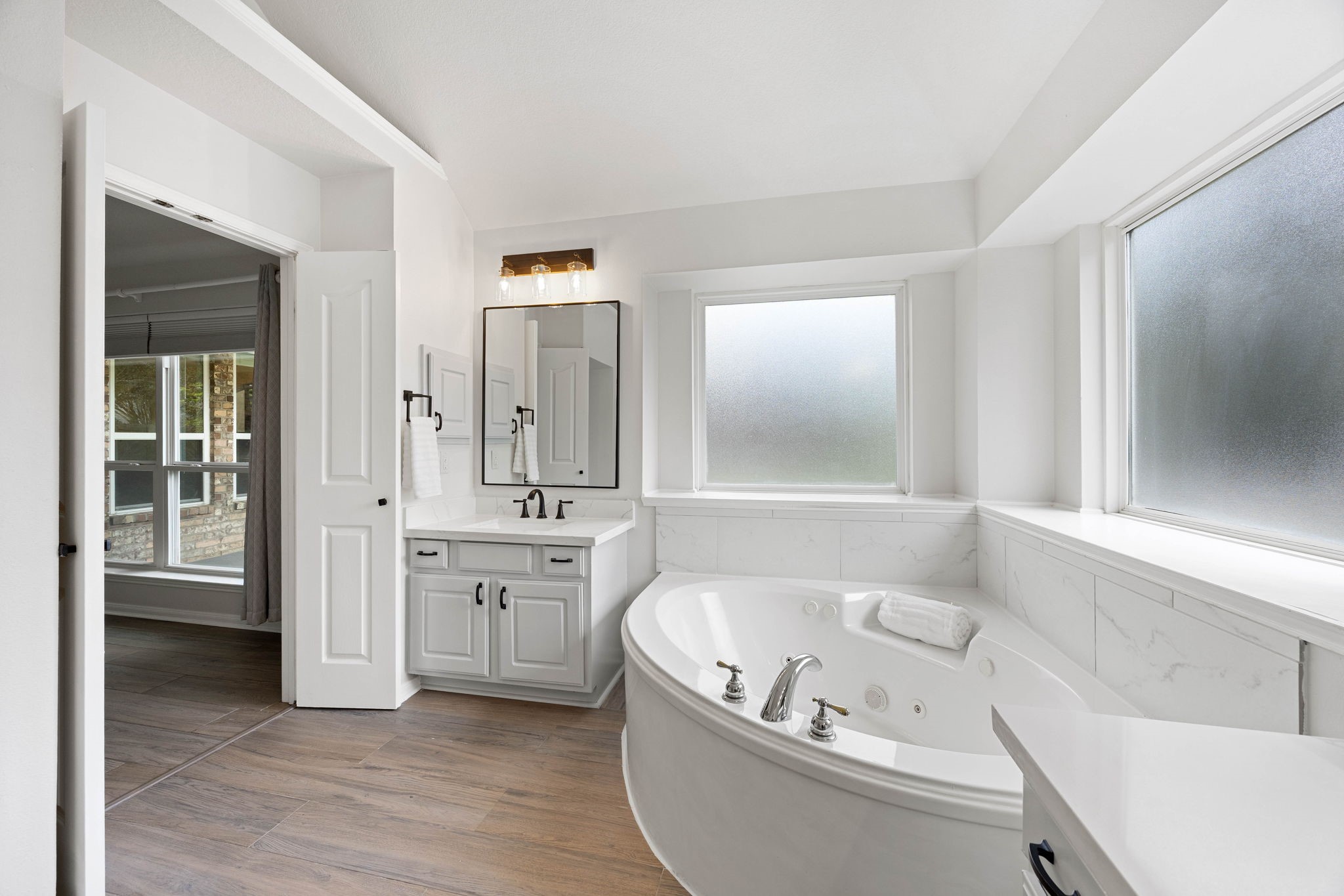 Additional primary bathroom view highlighting the soaking tub, dual vanity, large mirror, and bright finishes.