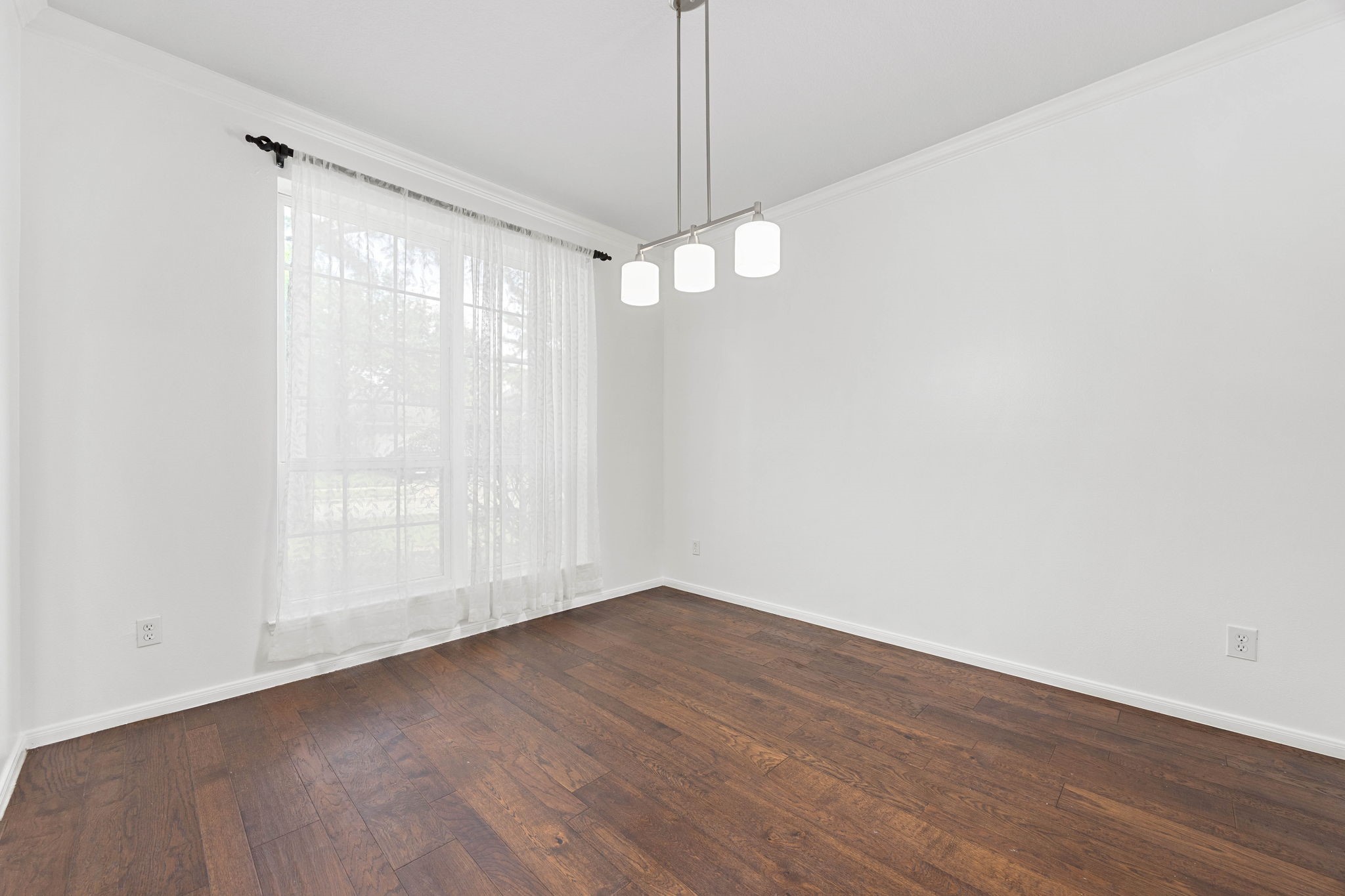 Formal dining area featuring rich wood flooring, contemporary lighting, and abundant natural light from large windows.