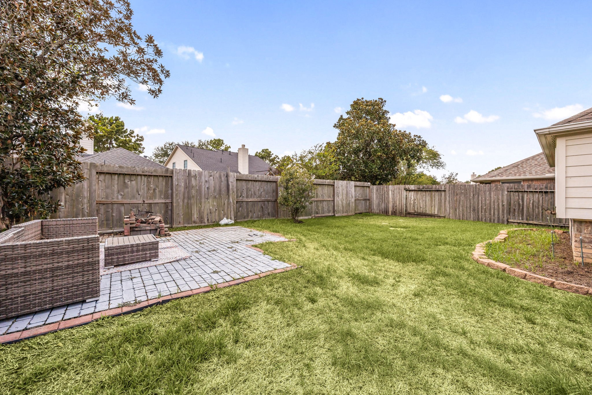 Wide backyard view showcasing the homes rear exterior, covered patio, and generous fenced lawn.