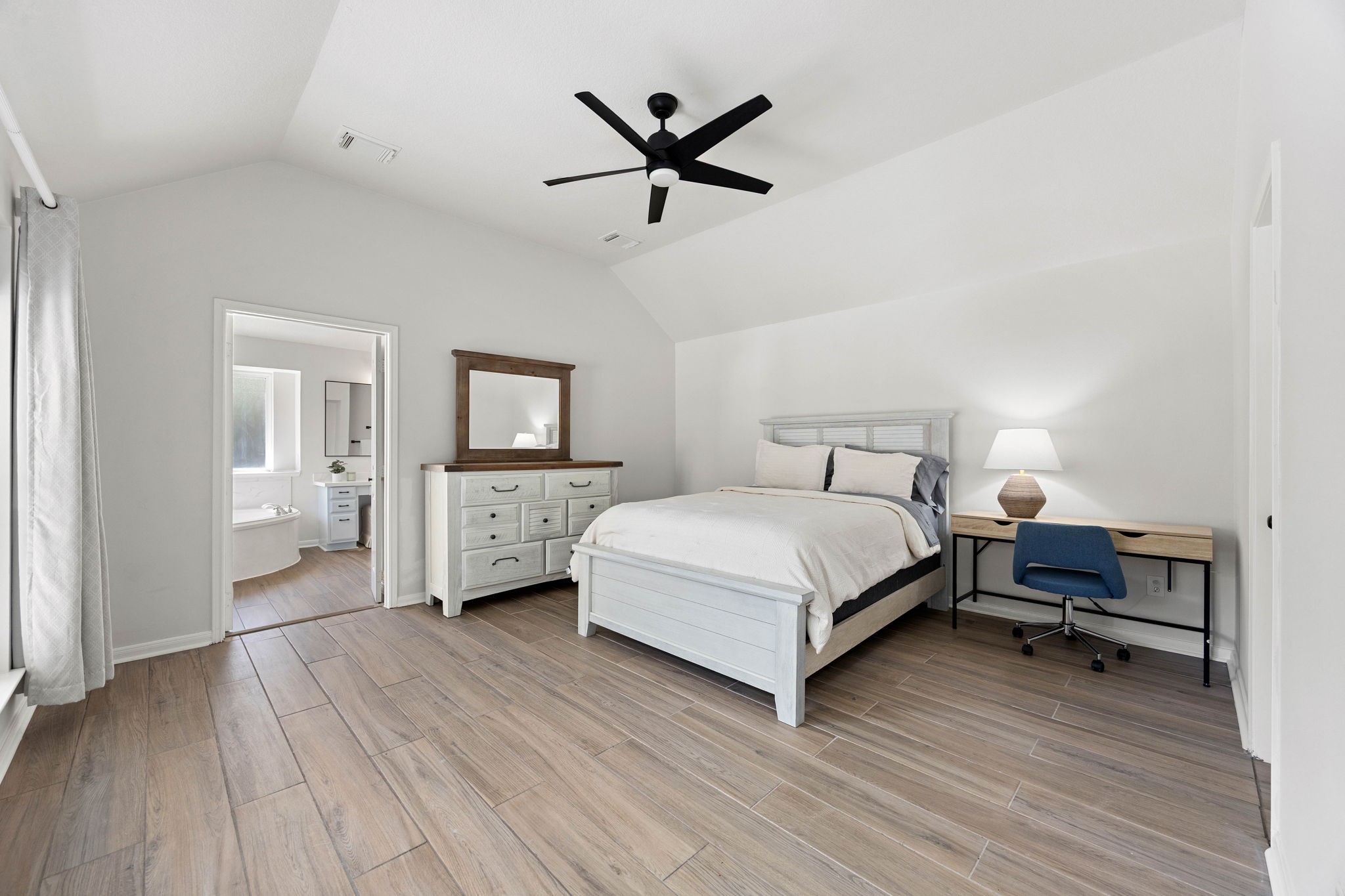 Spacious primary bedroom featuring a tray ceiling, ceiling fan, neutral finishes, and room for additional furnishings.